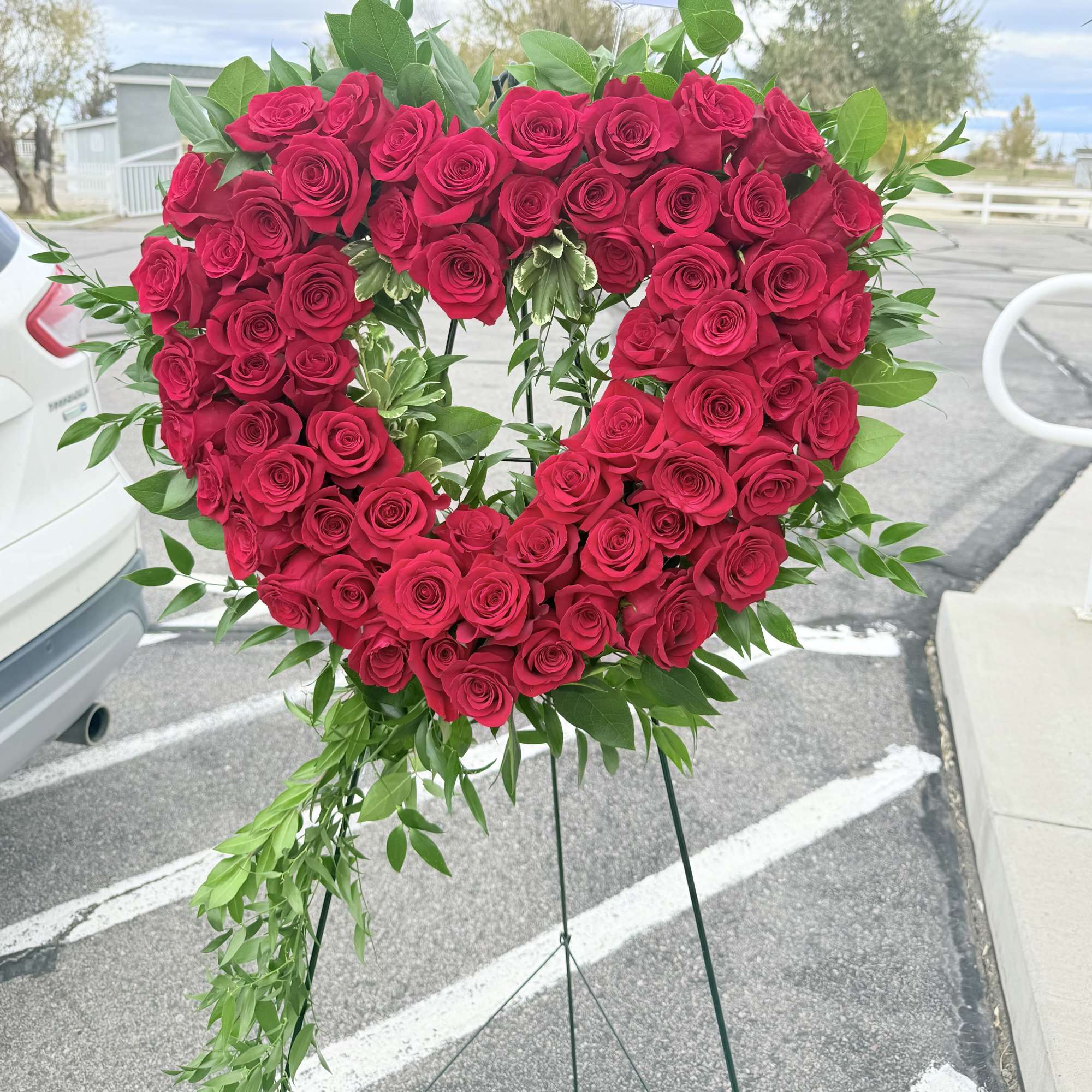 Heart-shaped arrangement of red roses with green foliage on a stand