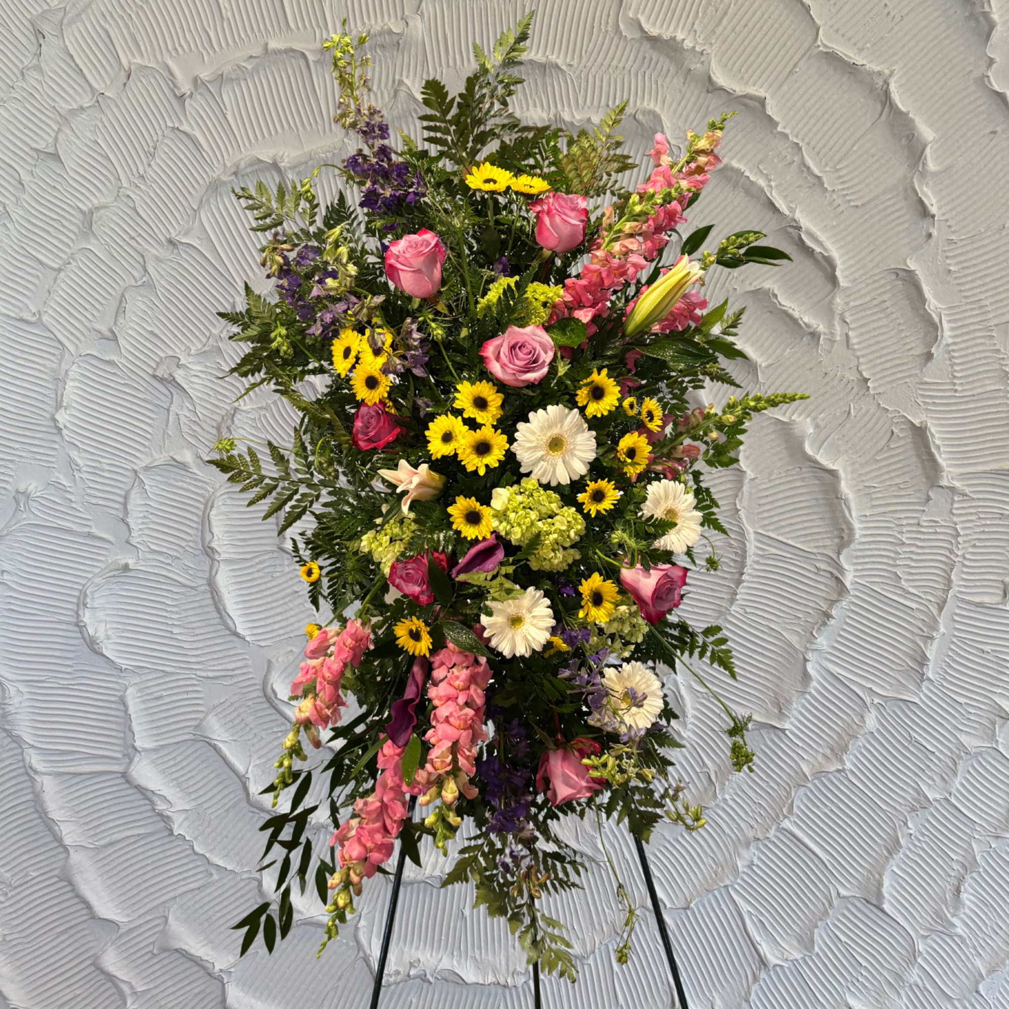 Standing floral spray with pink roses, yellow daisies, and purple blooms