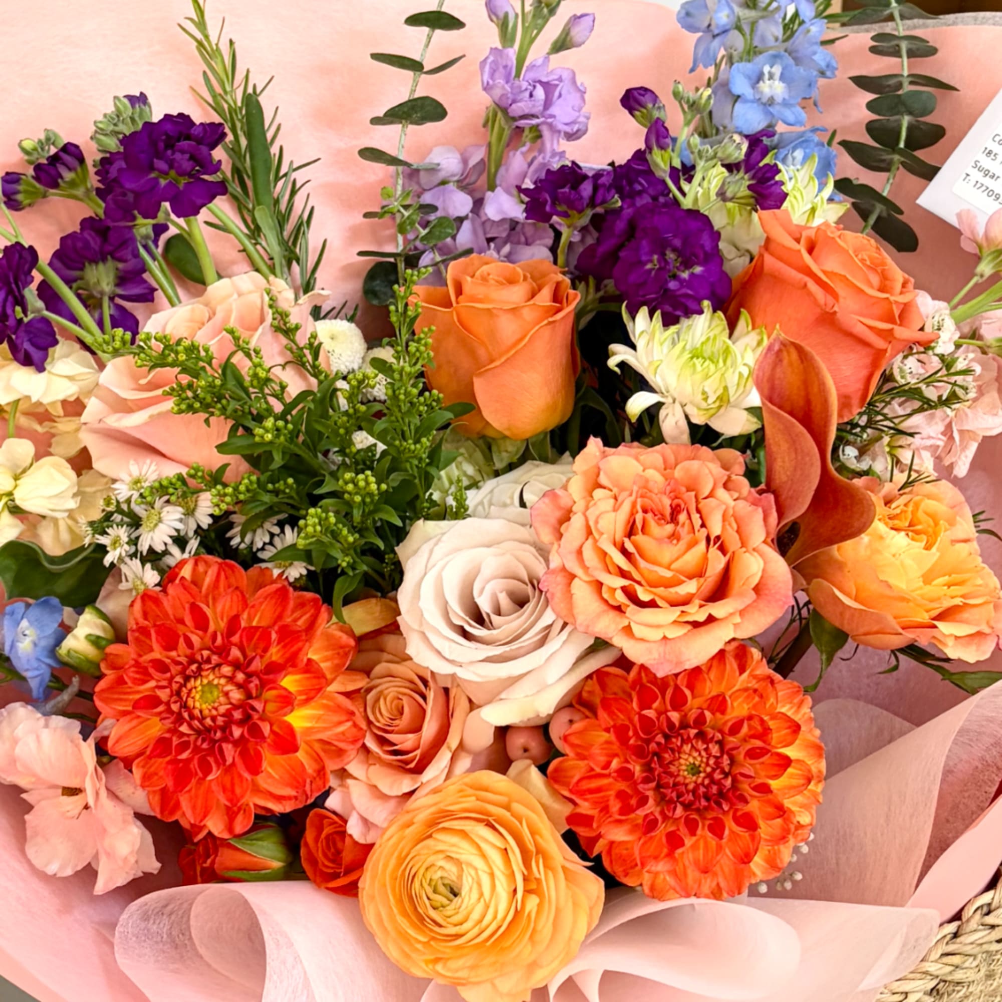 Mixed bouquet of orange, peach, purple, and white flowers wrapped in pink paper