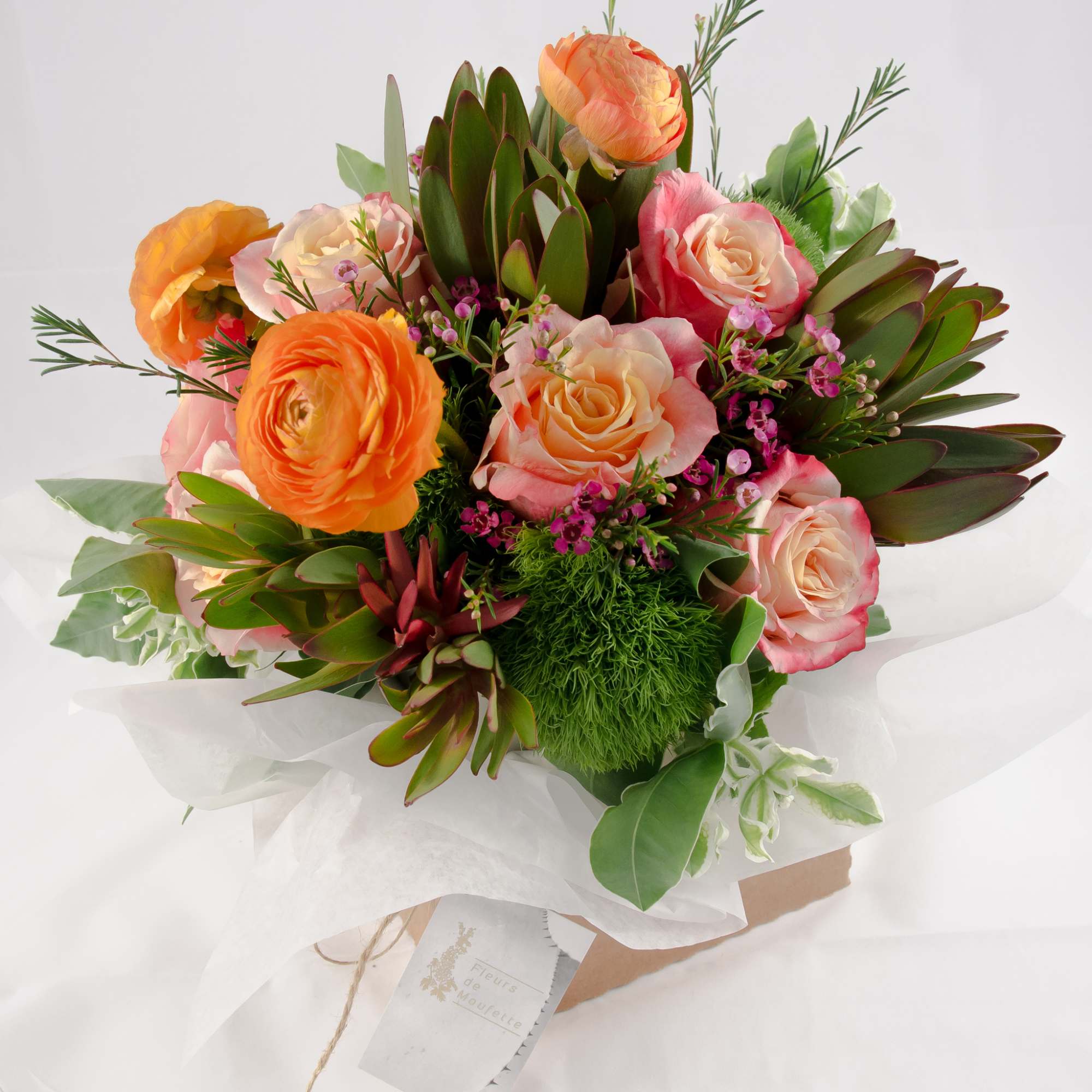 Bouquet of orange and pink roses with green foliage wrapped in white paper