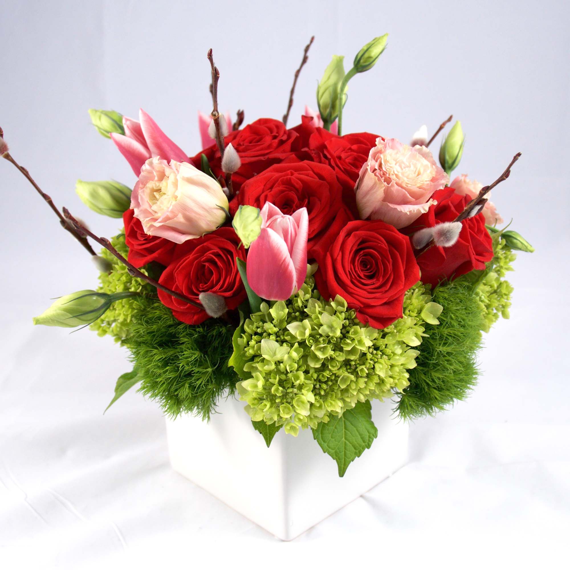 Red and pink roses arranged in a white square vase