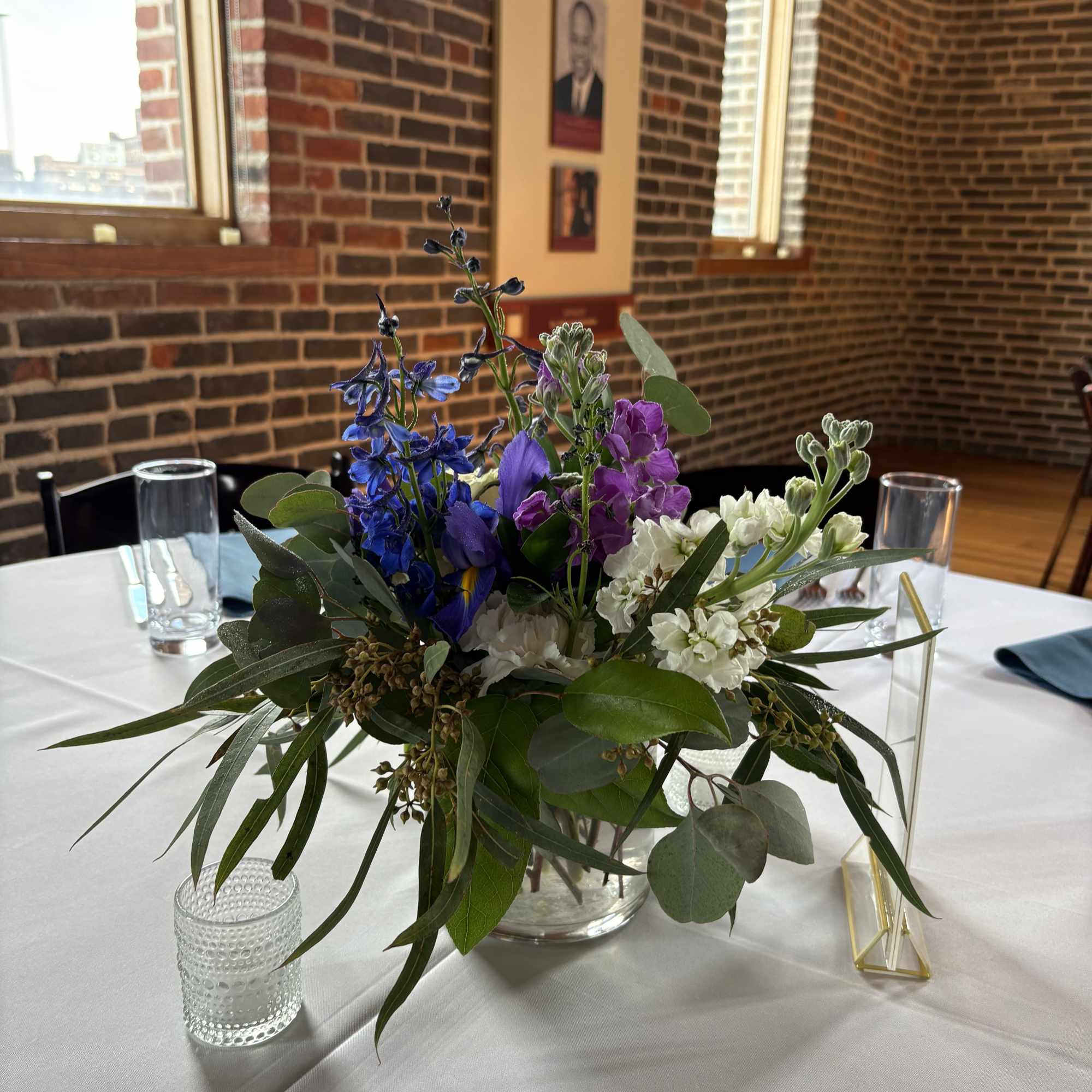 Mixed blue, purple, and white flowers in a clear glass vase on a table