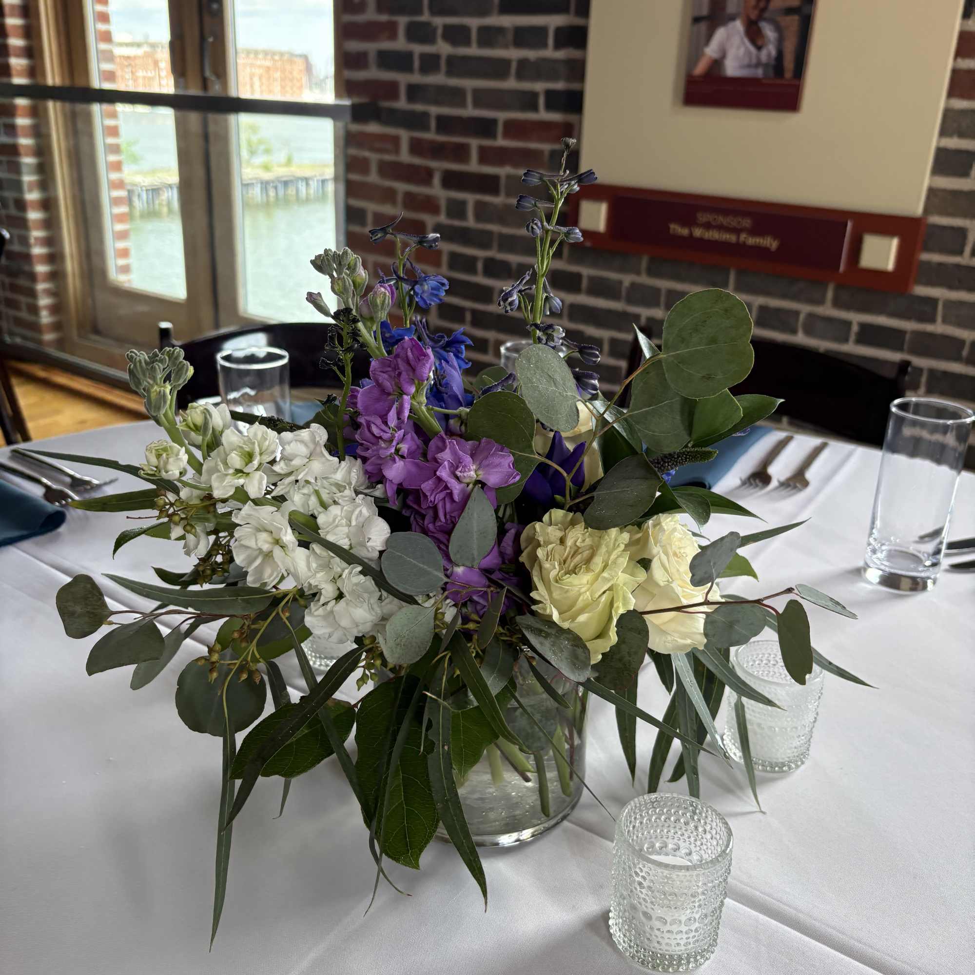 Mixed purple, white, and pale yellow flowers in a clear glass vase on a table