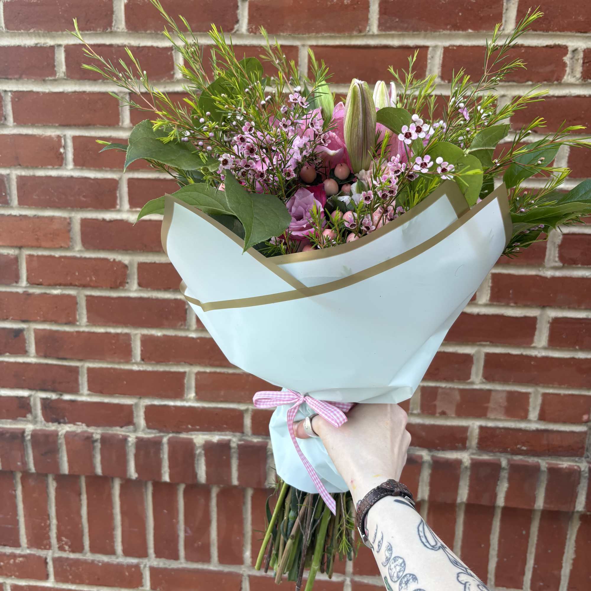 Handheld bouquet of pink flowers wrapped in pale blue paper with a ribbon