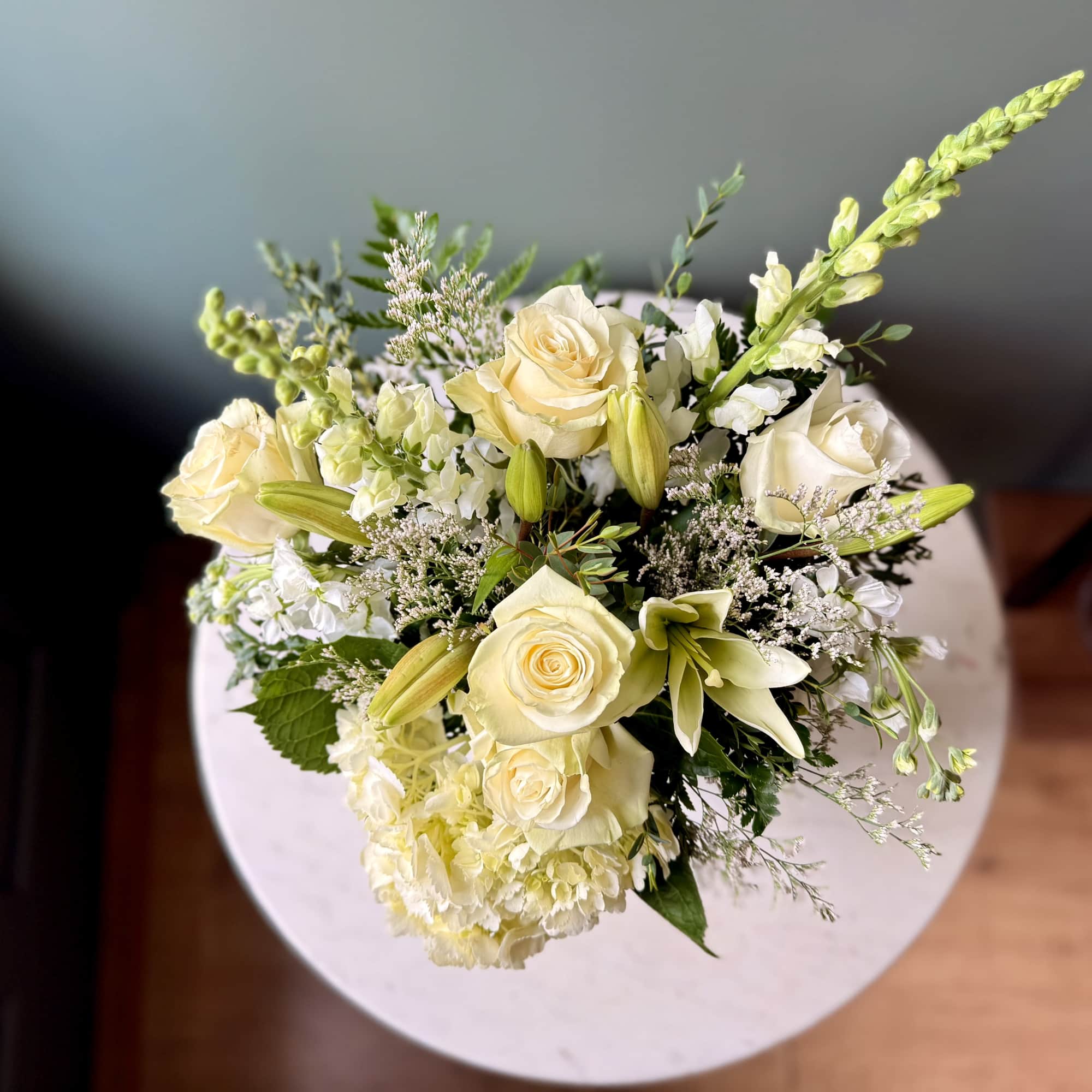 Arrangement of ivory roses, lilies, hydrangeas, and snapdragons in a soft, rounded design