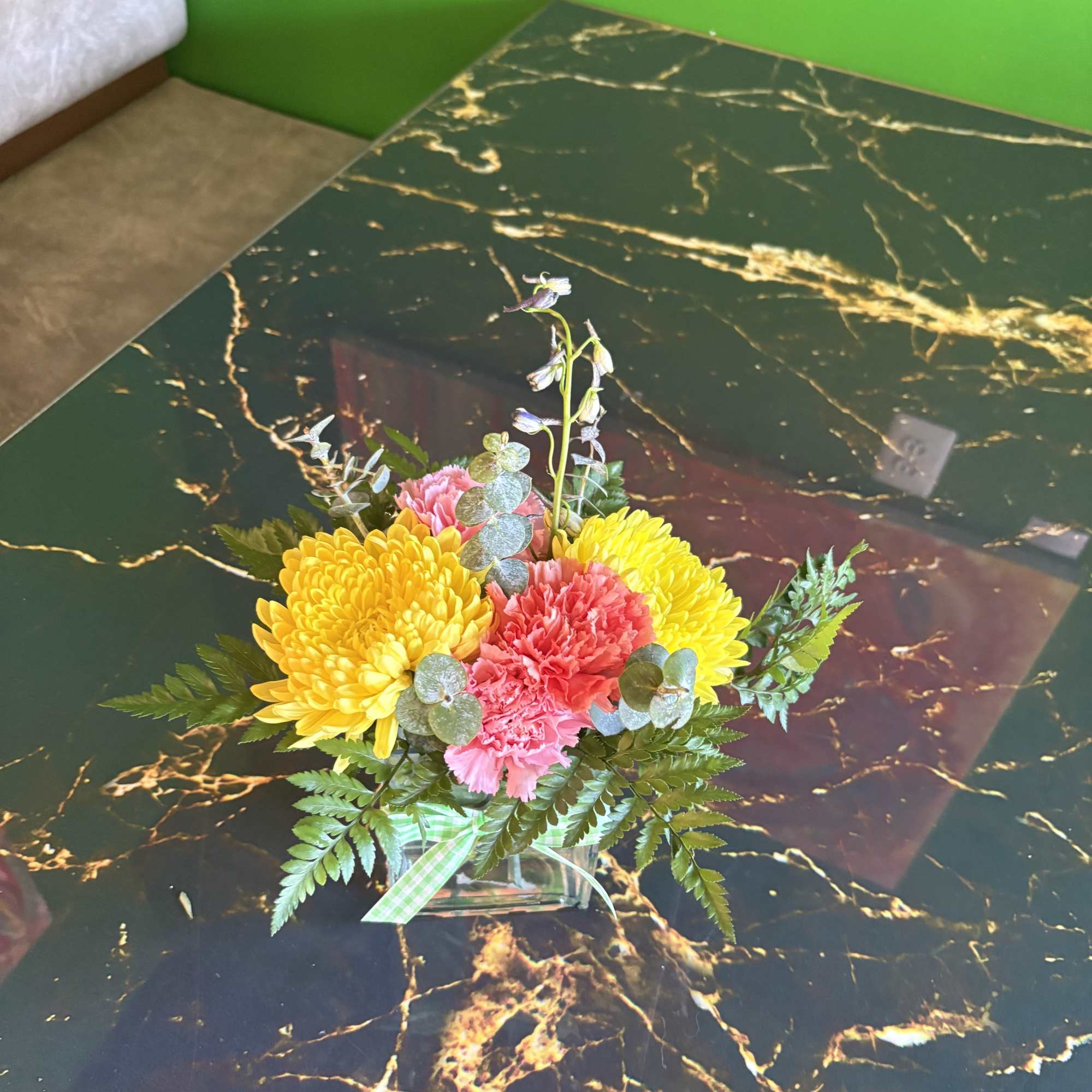 Small floral arrangement in a clear square vase with yellow and pink blooms