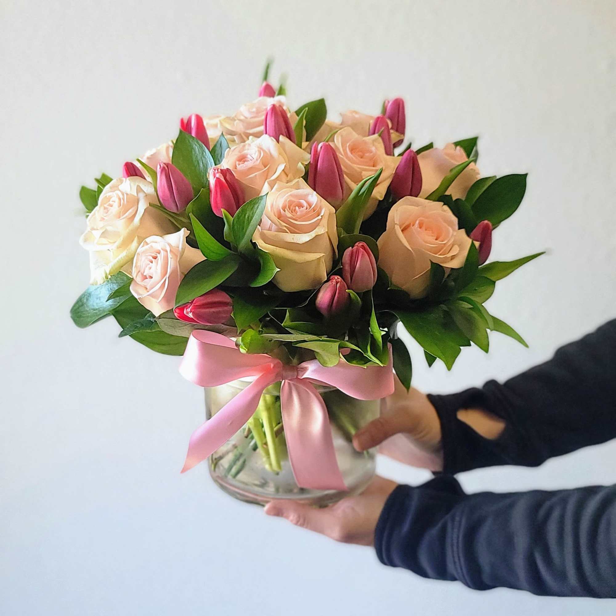 Bouquet of blush roses and pink tulips in a glass vase with a pink ribbon