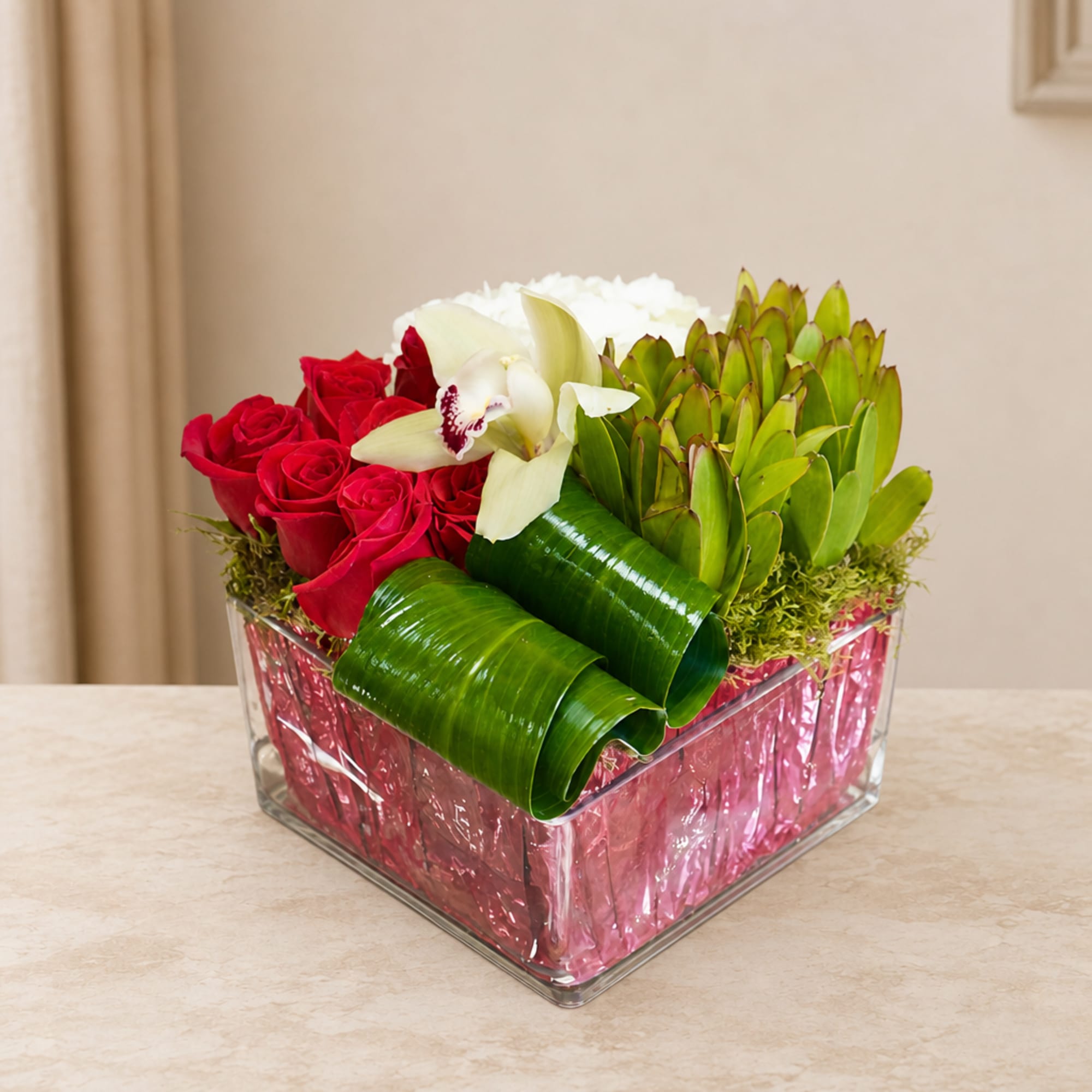 Red roses and white orchids arranged in a square glass vase