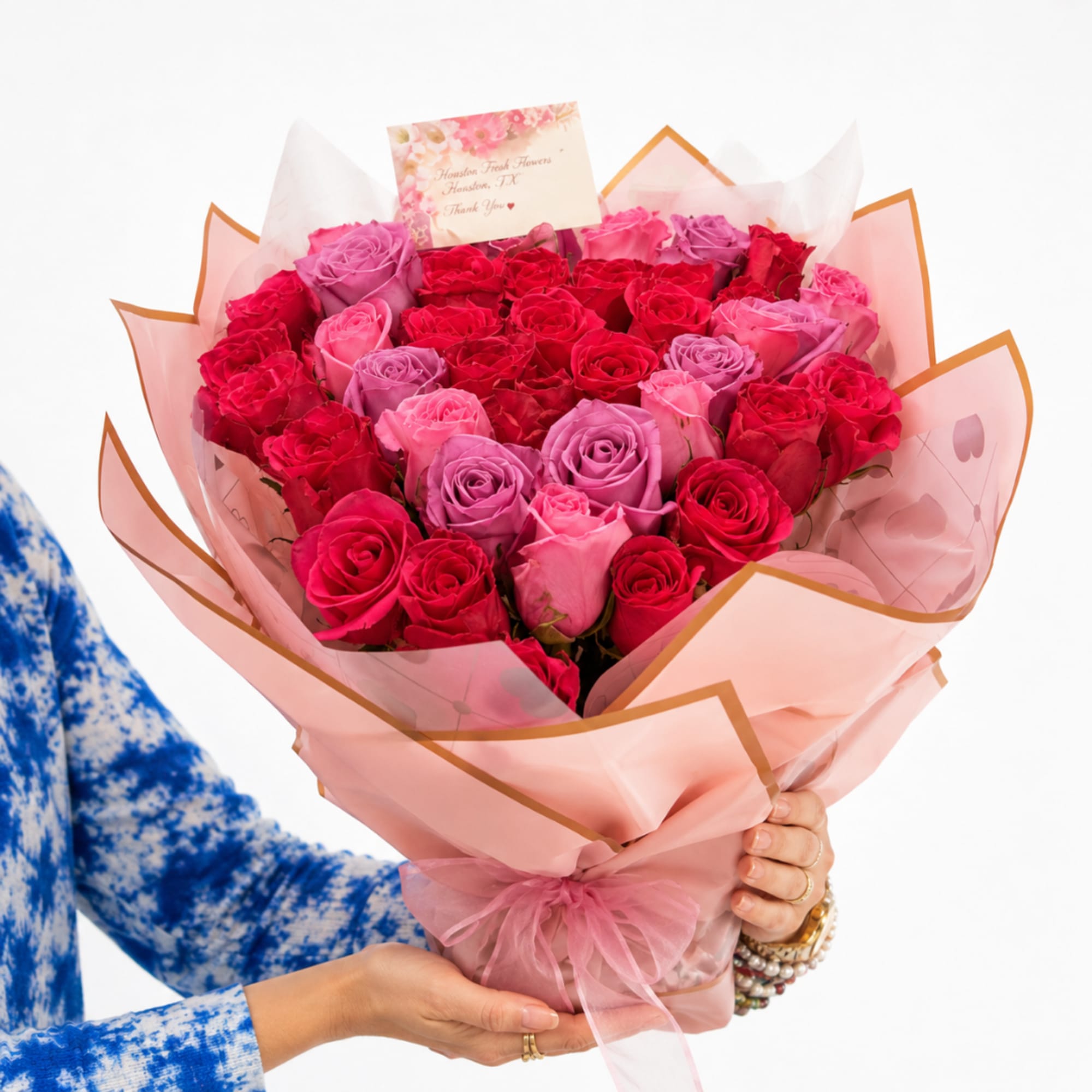 Handheld bouquet of pink, red, and lavender roses wrapped in pink paper