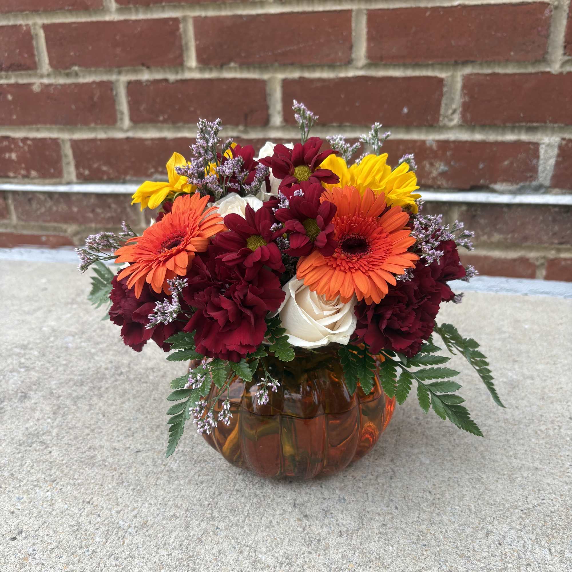 Mixed bouquet in an amber glass pumpkin vase with orange, yellow, burgundy, and white blooms