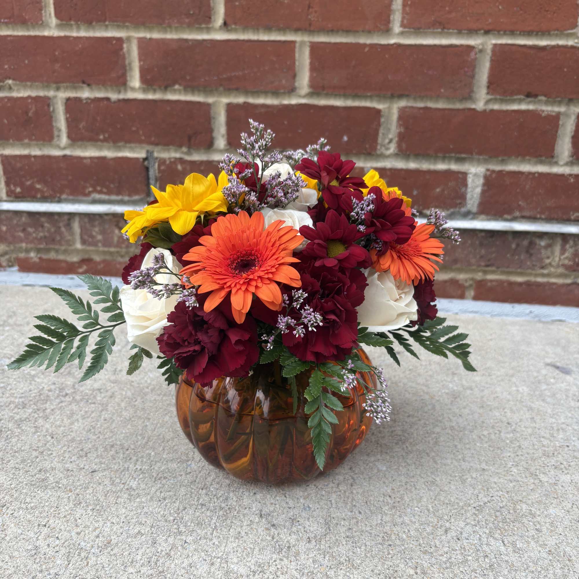 Mixed bouquet of orange, yellow, burgundy, and white flowers in an amber glass vase