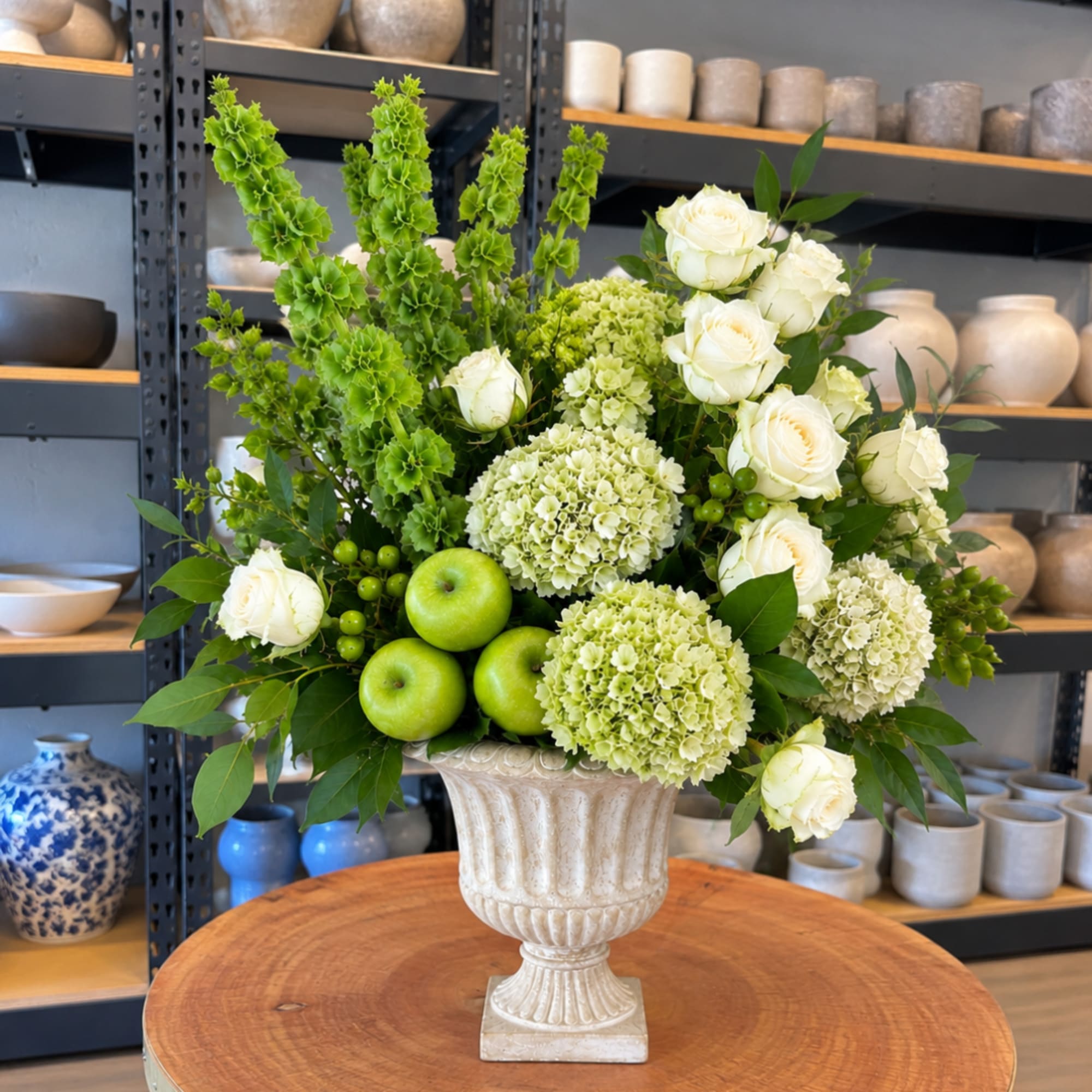 White roses and green hydrangeas in a white urn vase with green apples