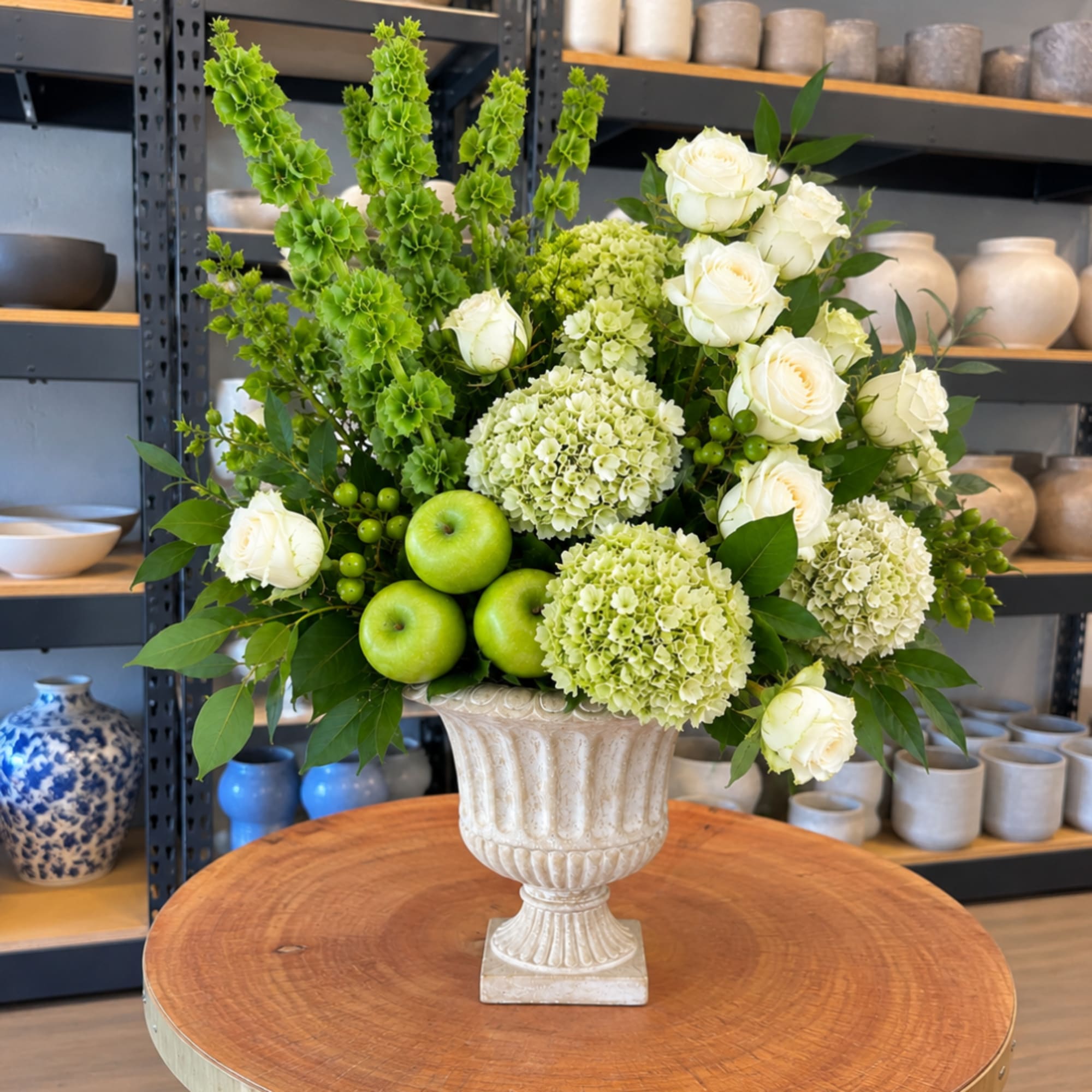 White roses and green hydrangeas in a decorative urn with green apples