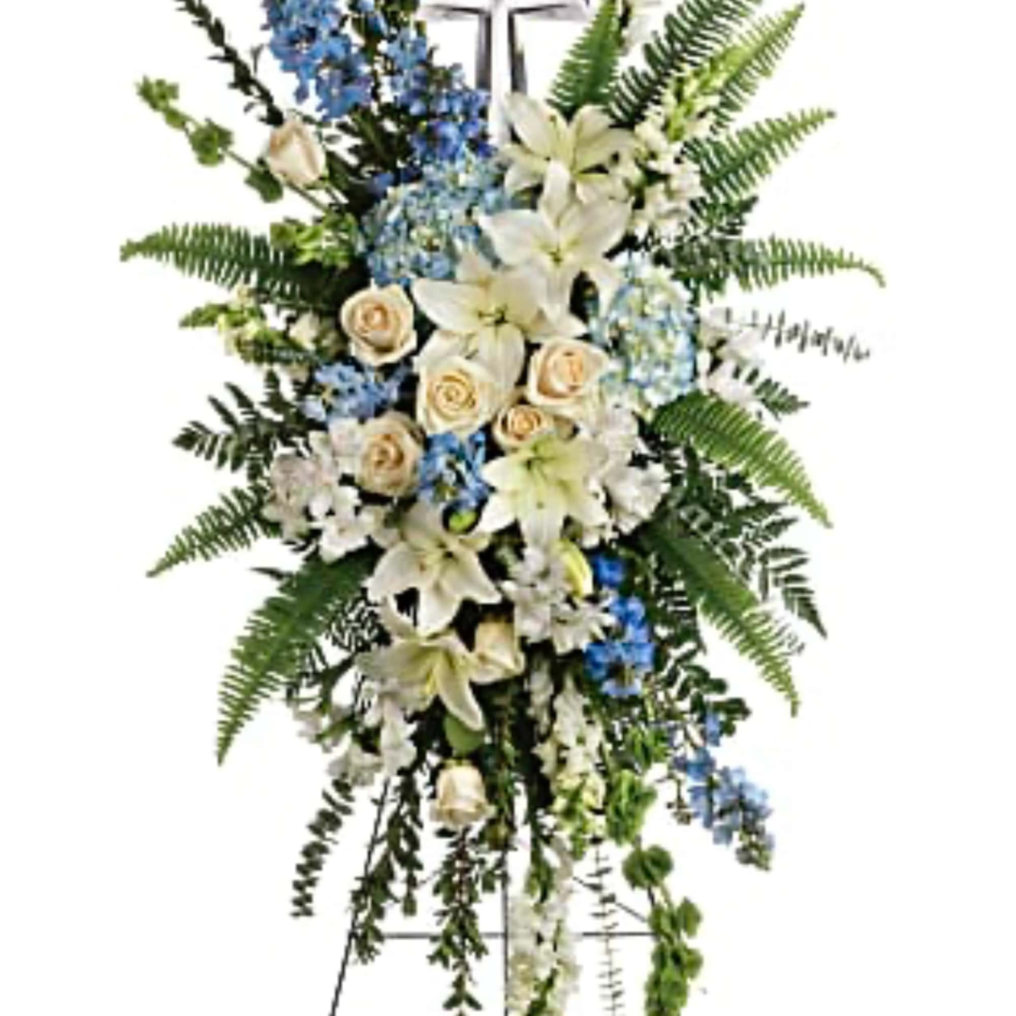 Standing floral spray with white lilies, cream roses, and blue flowers around a cross