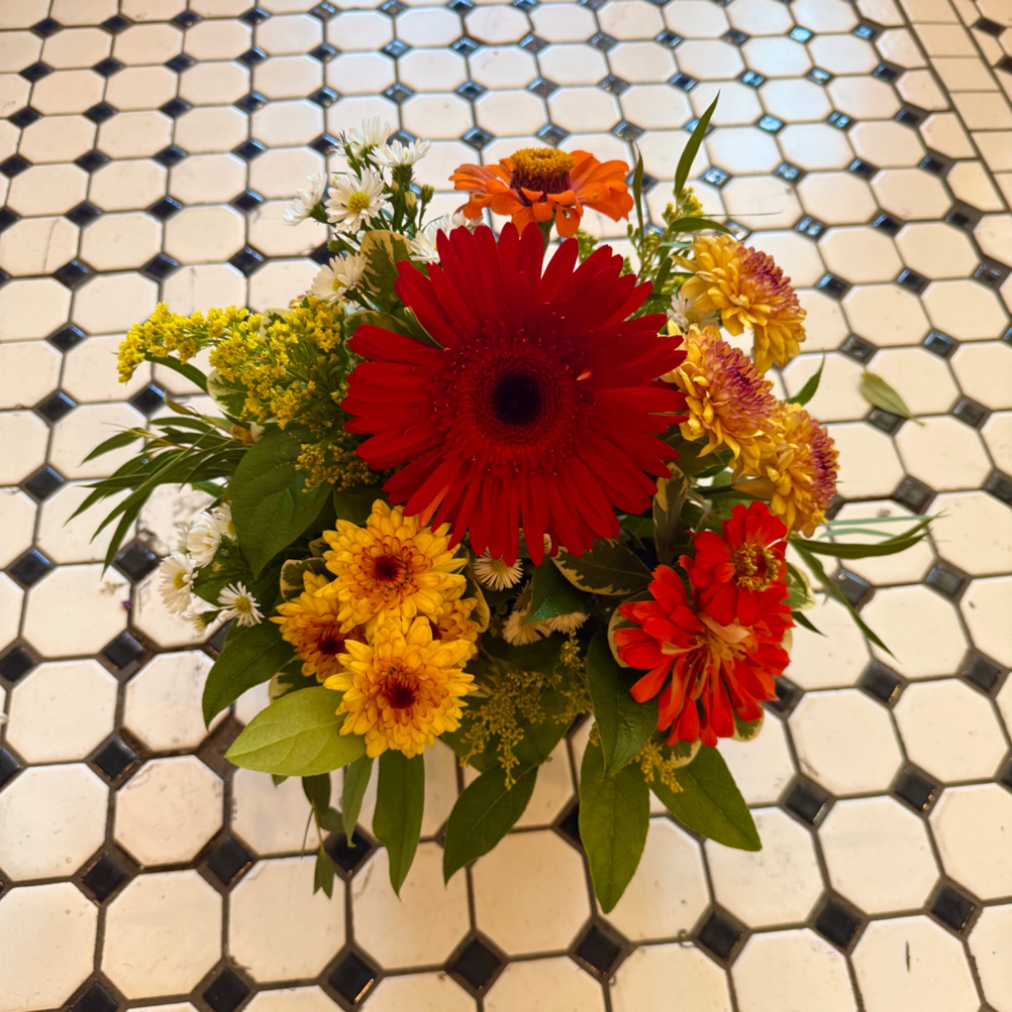 Mixed bouquet with red, orange, and yellow daisies on a tiled floor