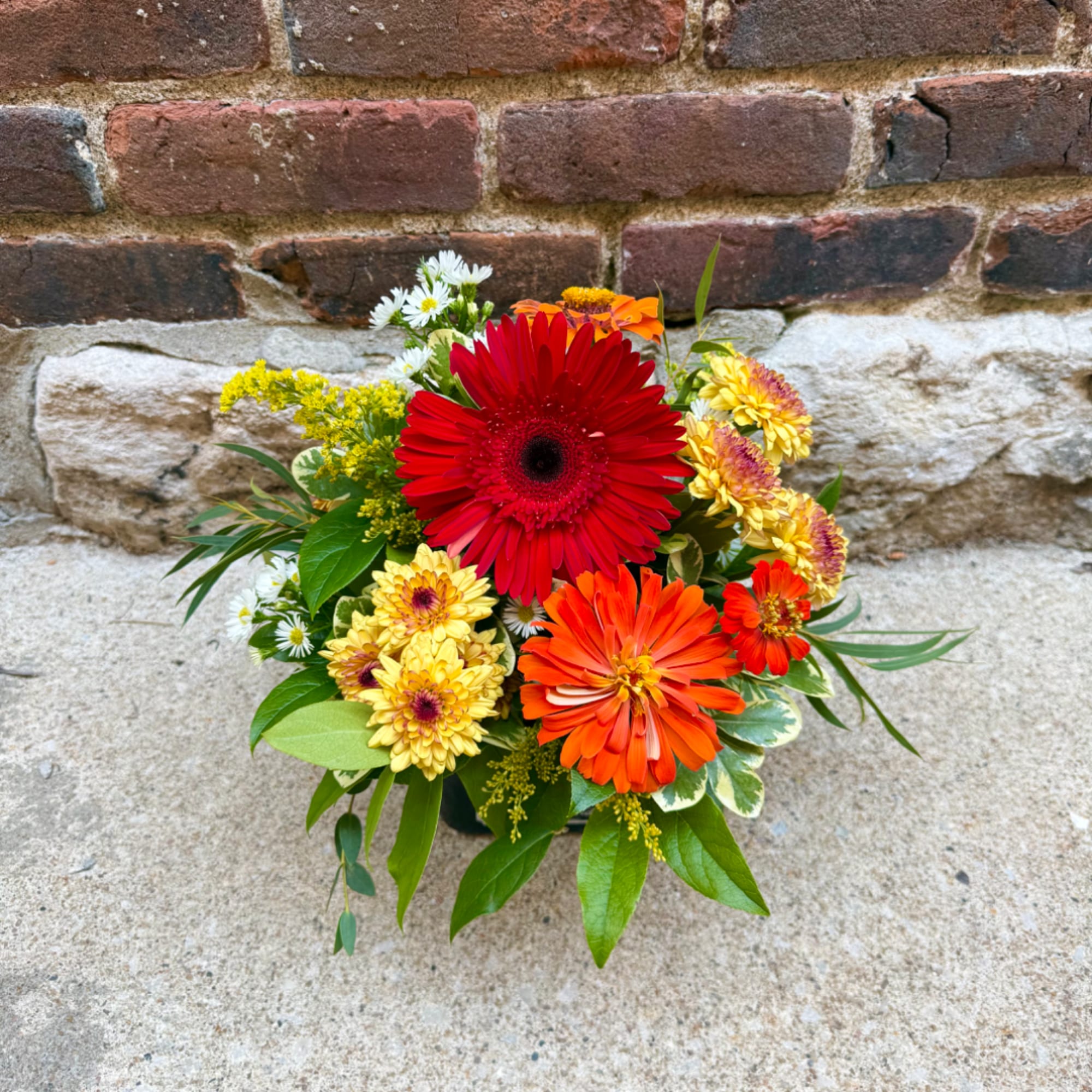 Mixed bouquet with red, orange, and yellow daisies in a vase