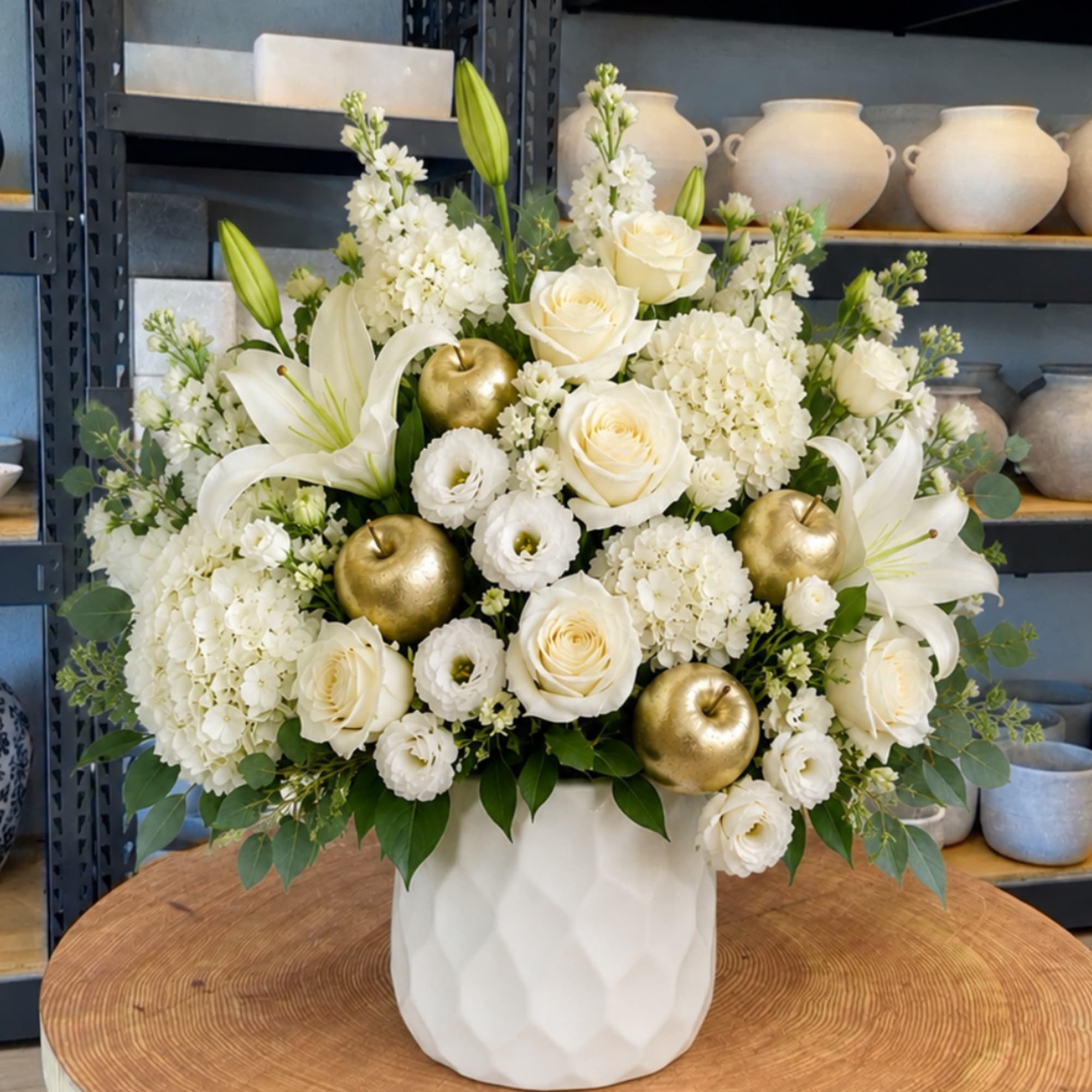 White floral arrangement with roses, lilies, and gold apple accents in a white vase