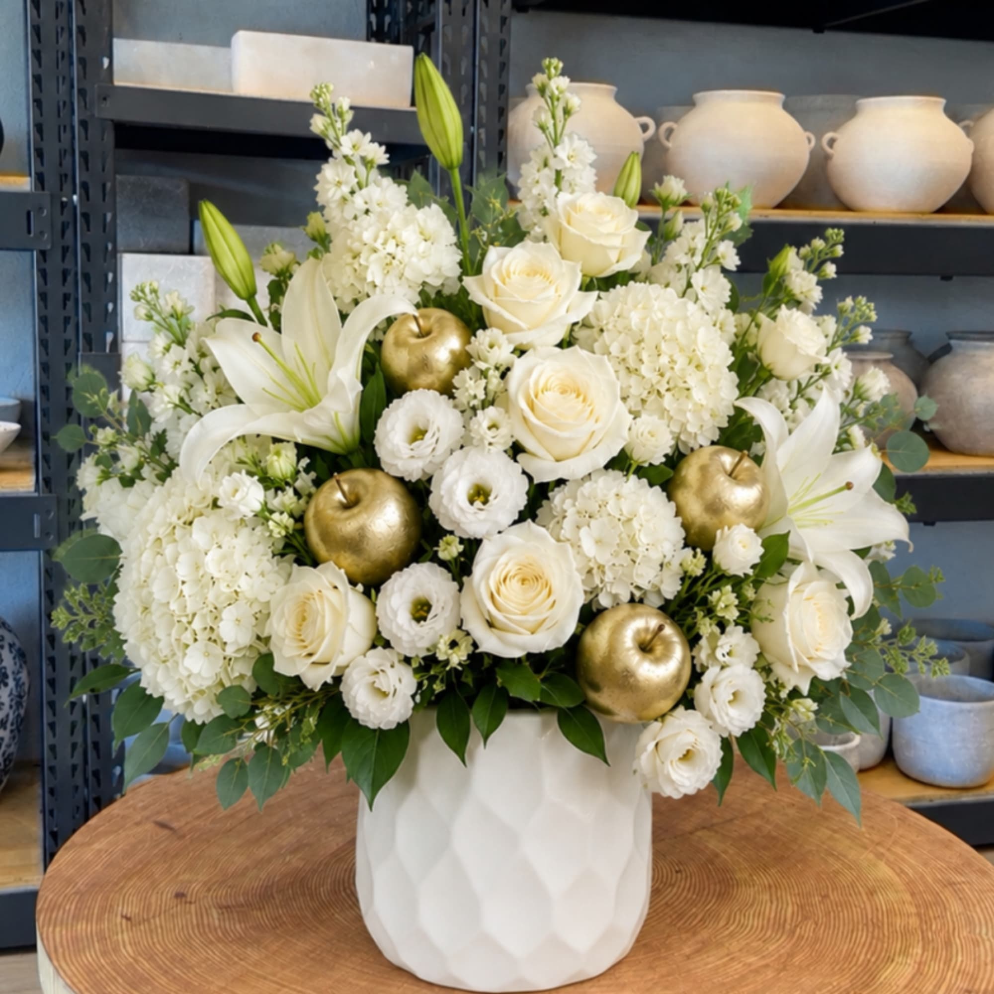 White floral arrangement in a white vase with gold apple accents