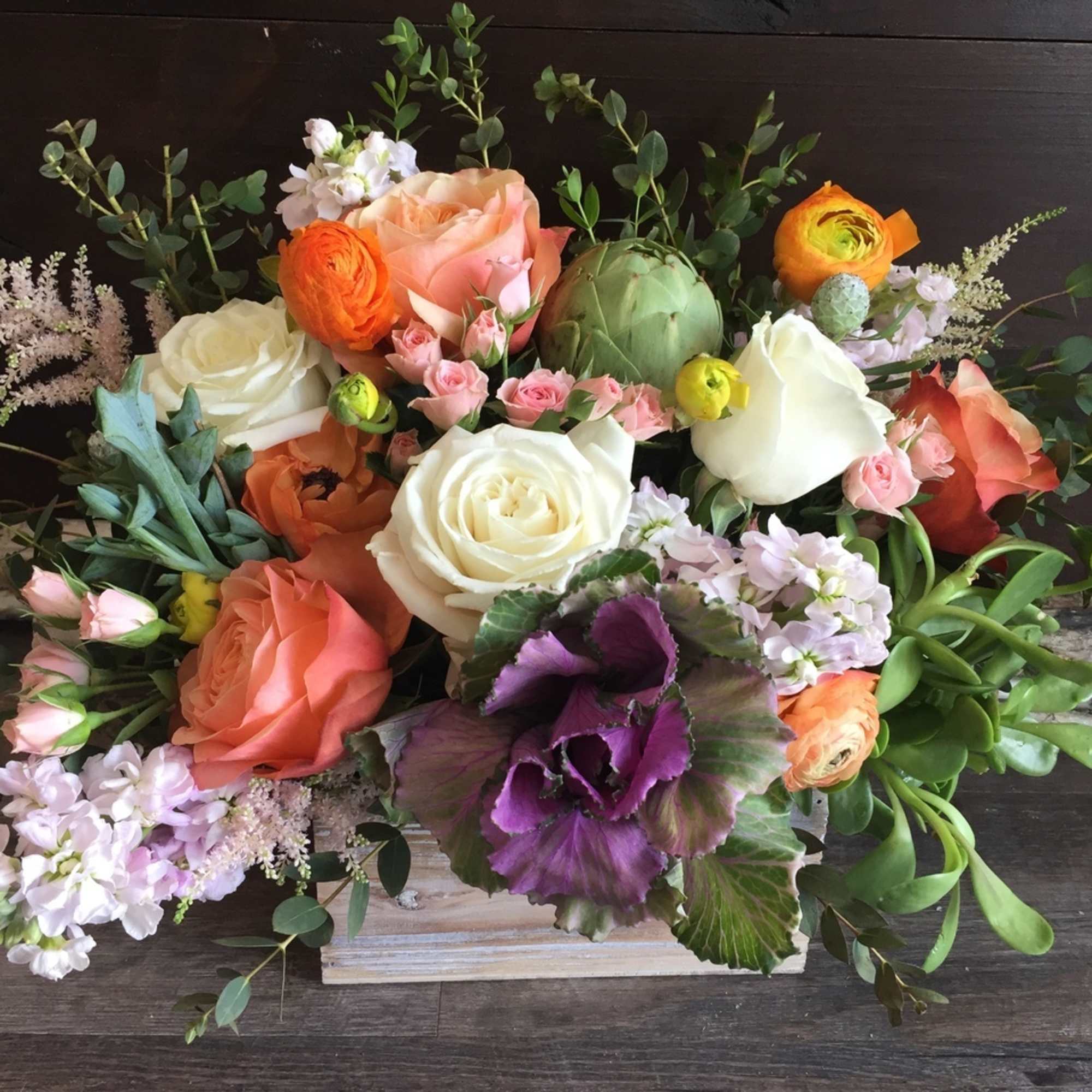 Low arrangement of peach and white roses with ranunculus, stock, succulents and kale in a rustic wooden box