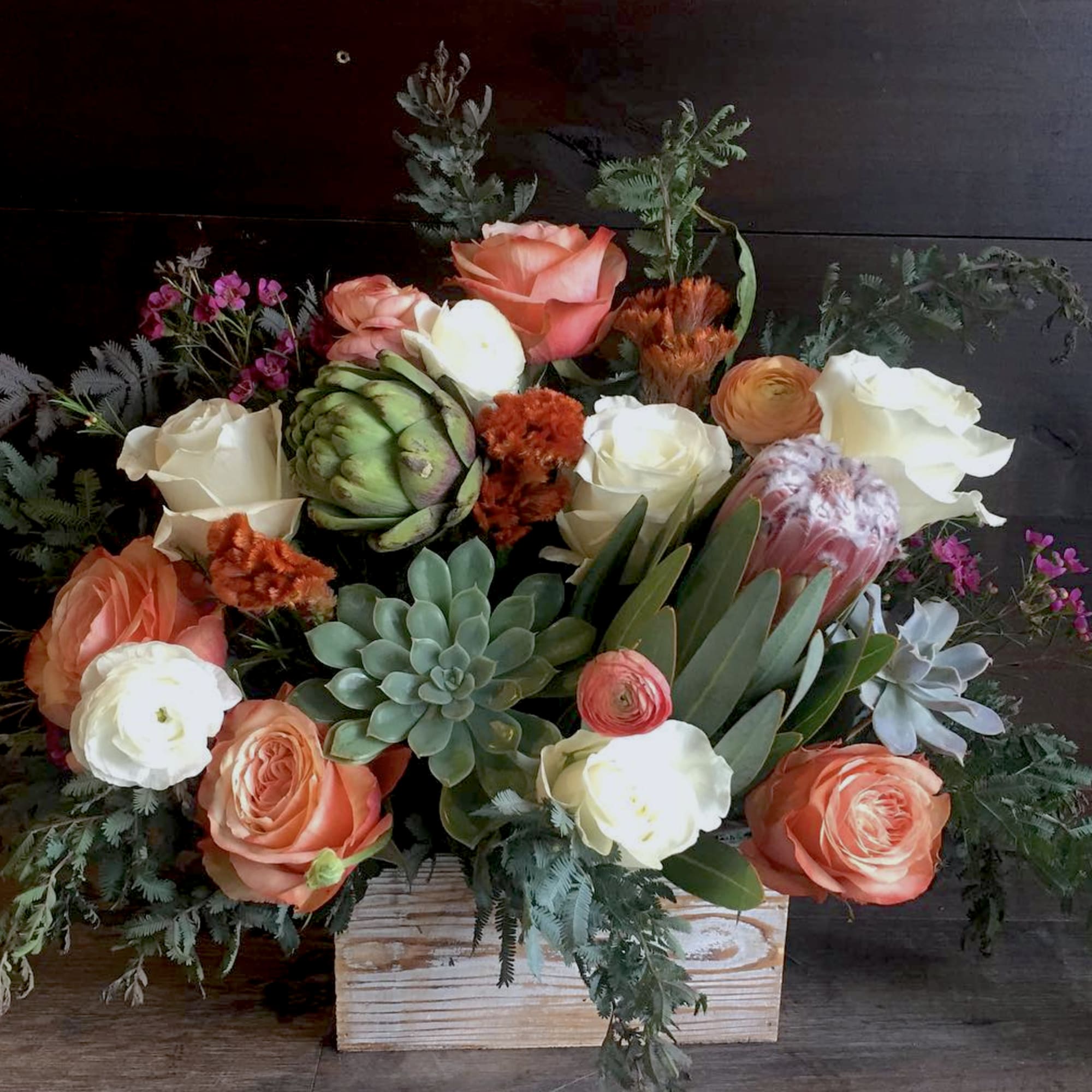 Low wooden box arrangement with peach and white roses, succulents, protea, and mixed accent blooms