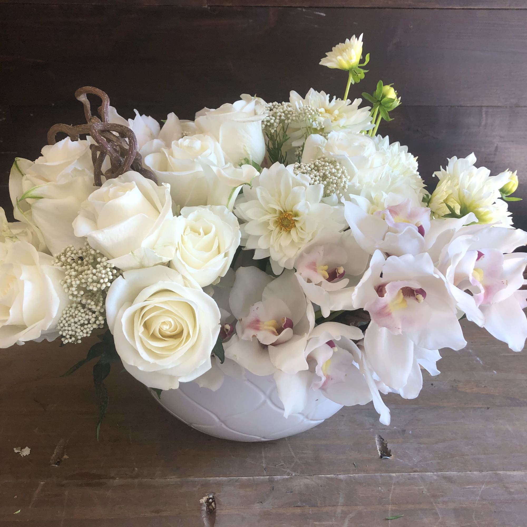 White roses and orchids arranged in a white bowl vase
