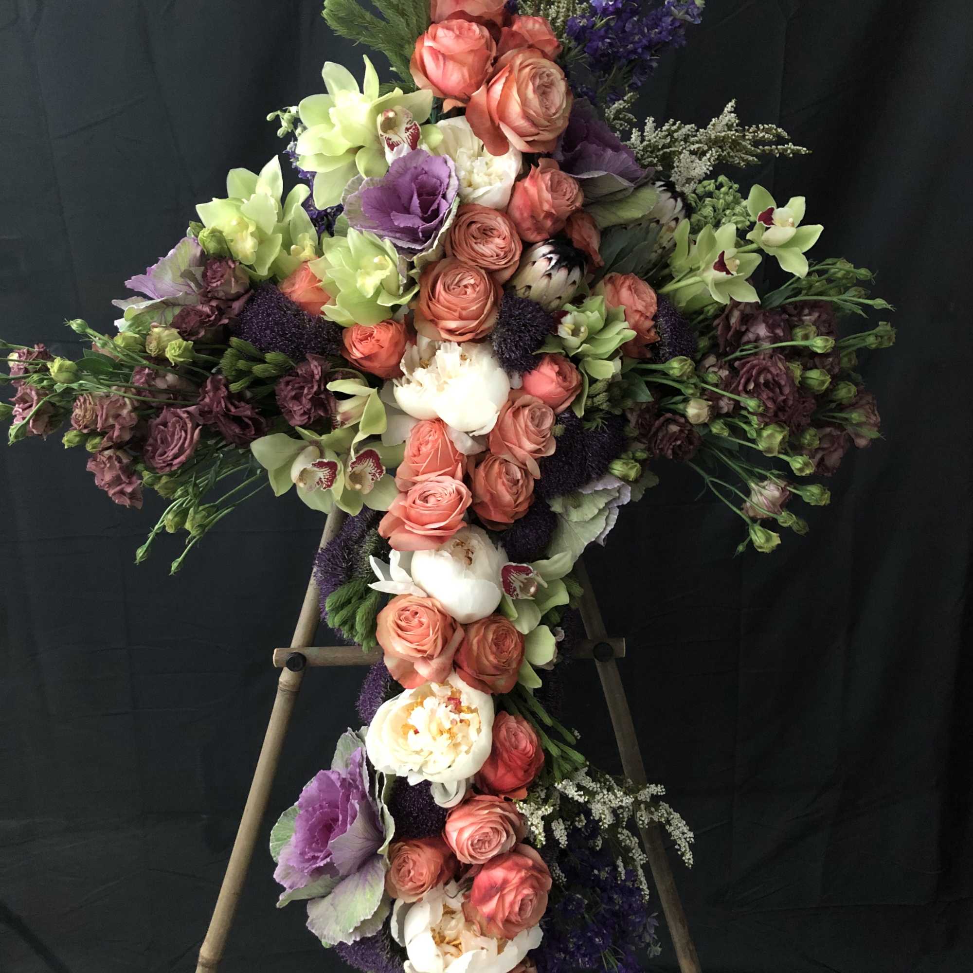 Large floral cross with pink roses, white blooms, and purple flowers