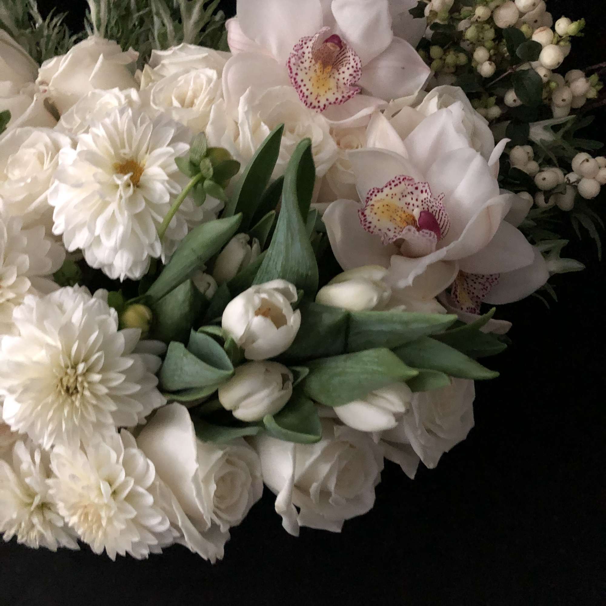 White bouquet with roses, orchids, and daisies on a dark background