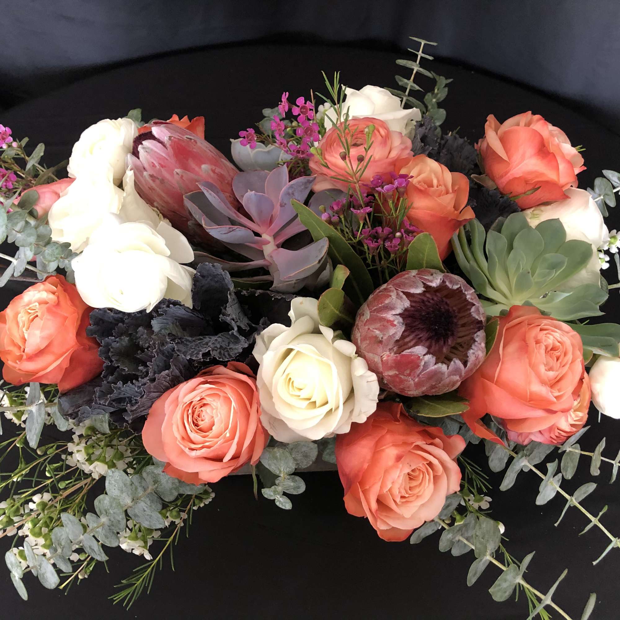 Low arrangement of orange and white roses with protea and succulents in a lush centerpiece