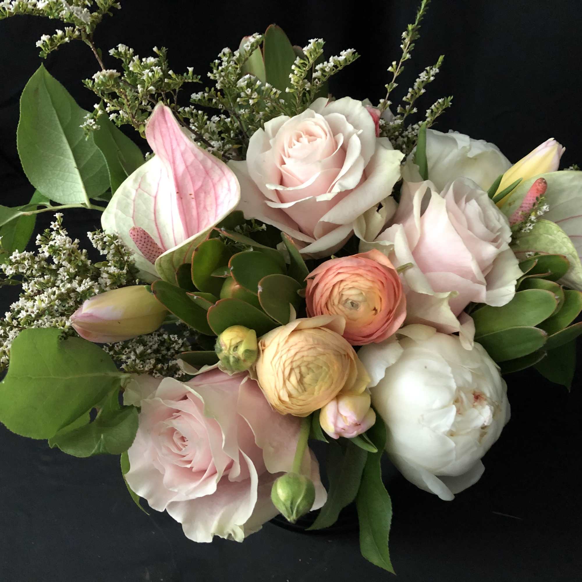 Bouquet of pale pink and white roses with ranunculus and anthurium on a black background