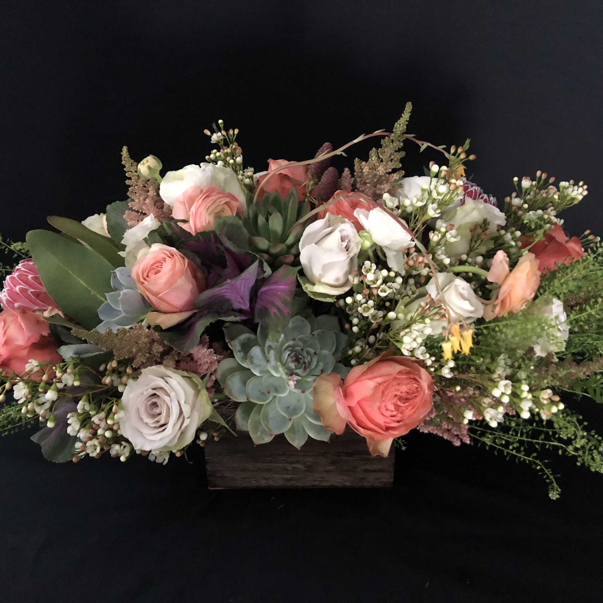 Low arrangement of pink and white roses with succulents in a wooden box