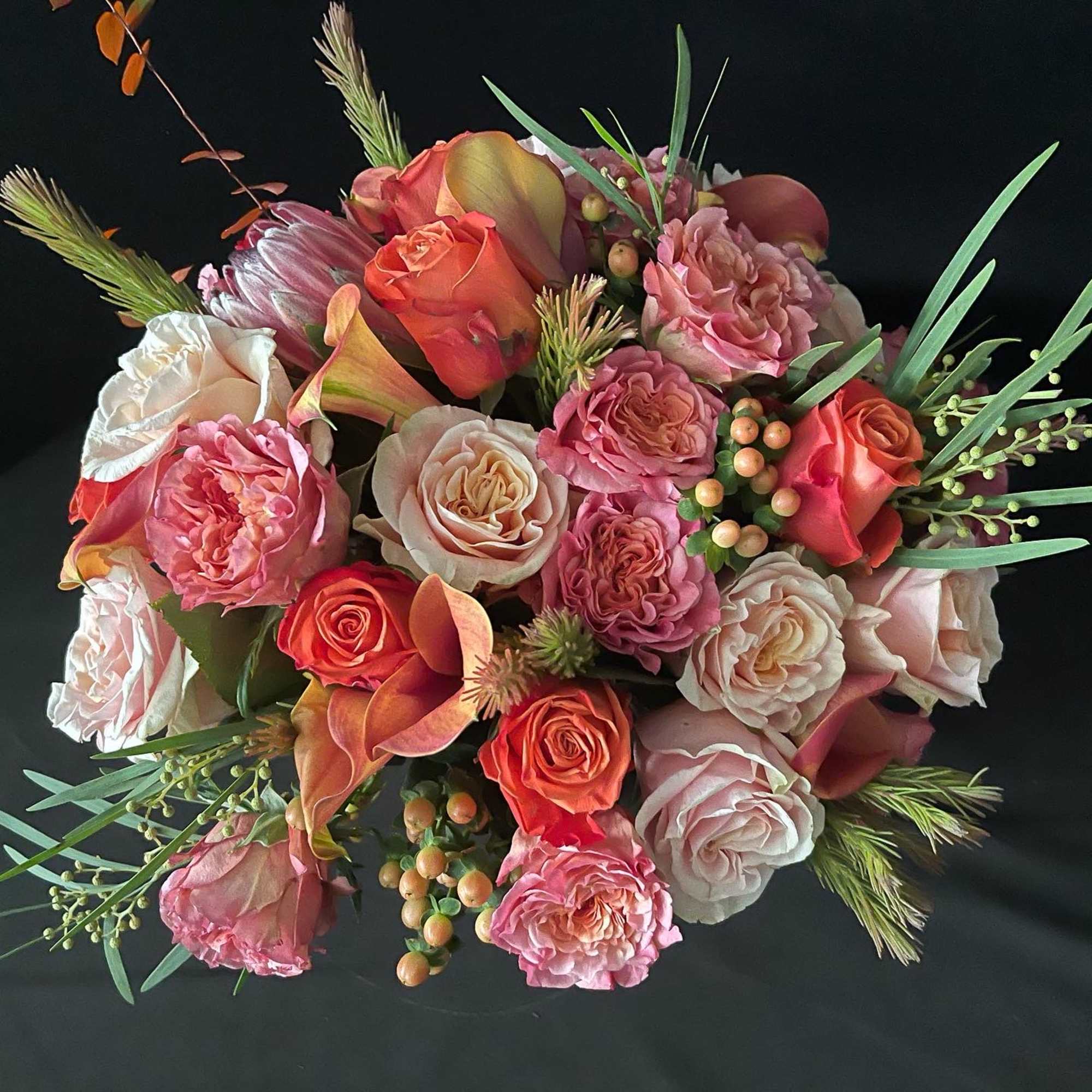 Bouquet of pink and coral roses with calla lilies on a black background