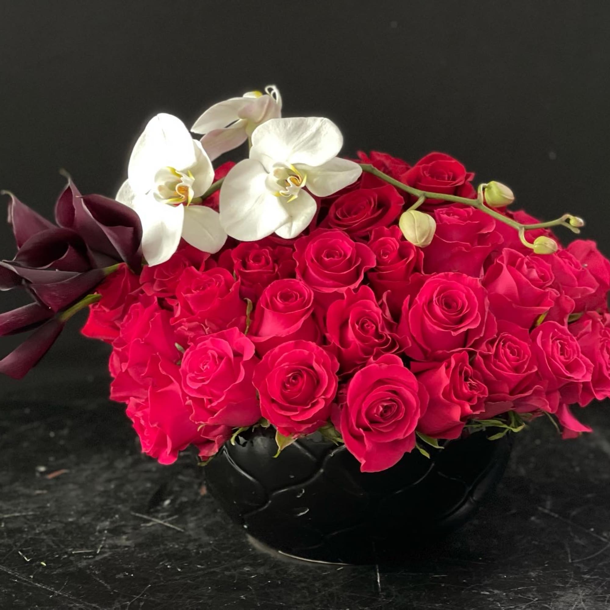 Pink rose arrangement with white orchids in a black vase
