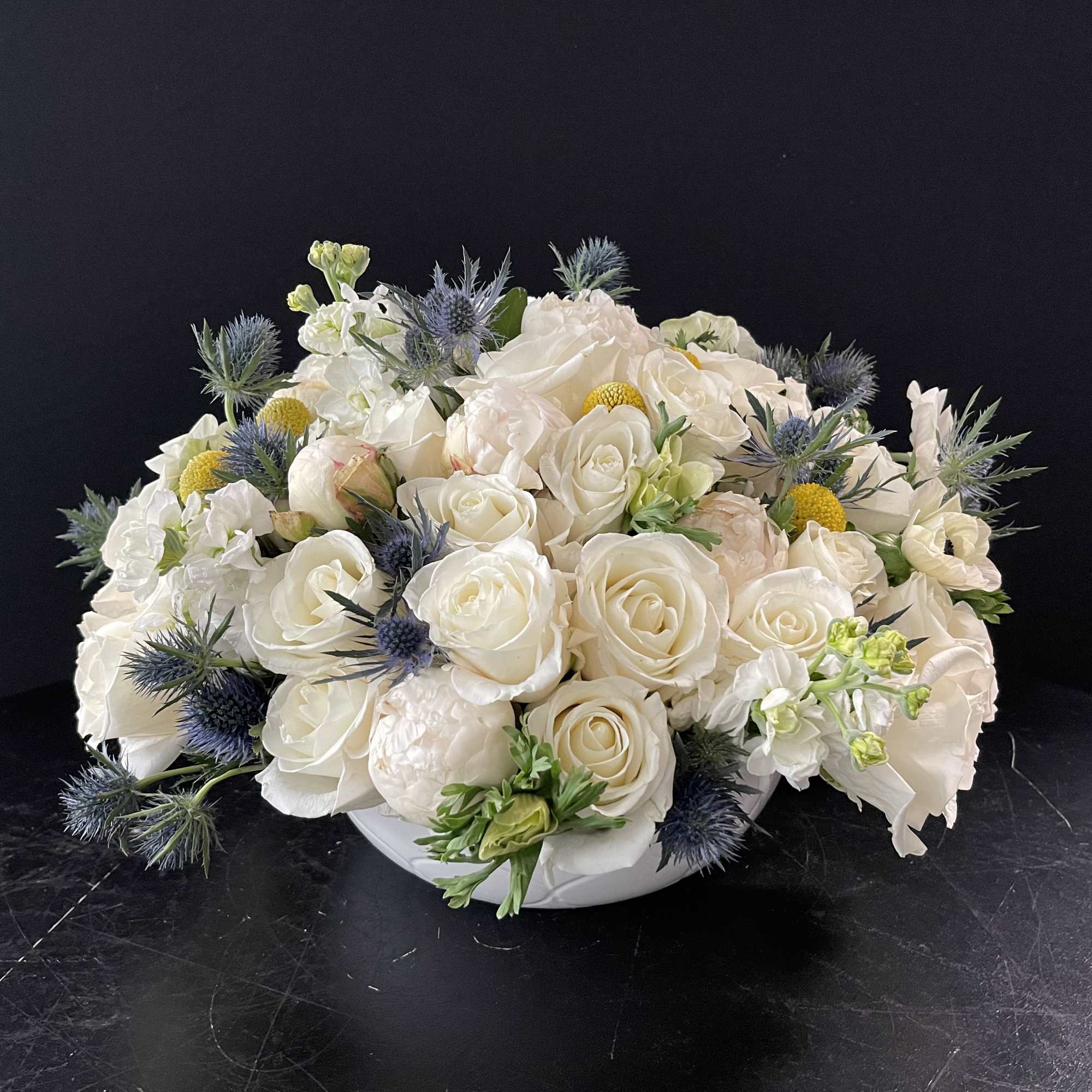 White rose arrangement with blue thistle in a low white bowl