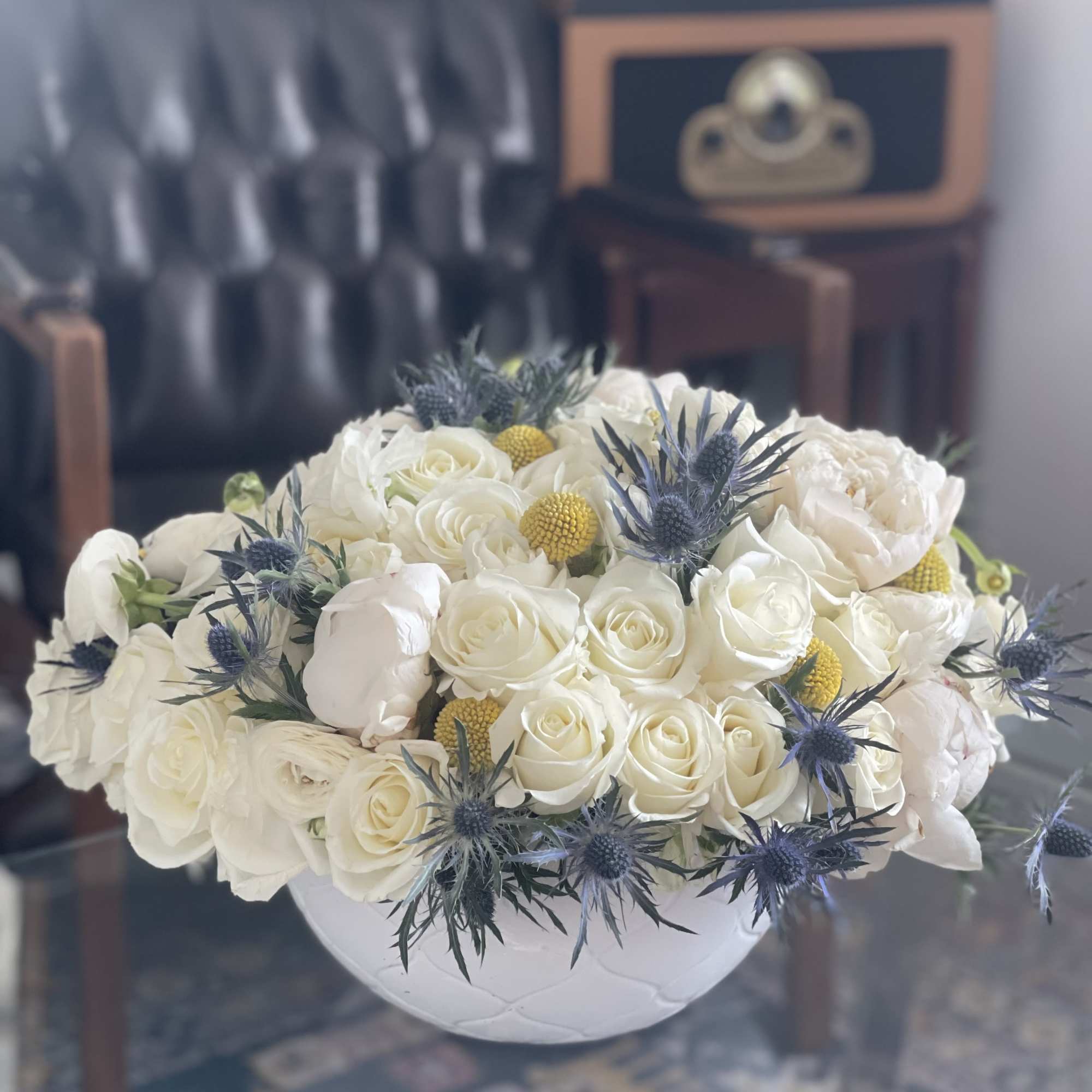 White rose bouquet in a round white vase with blue thistle accents