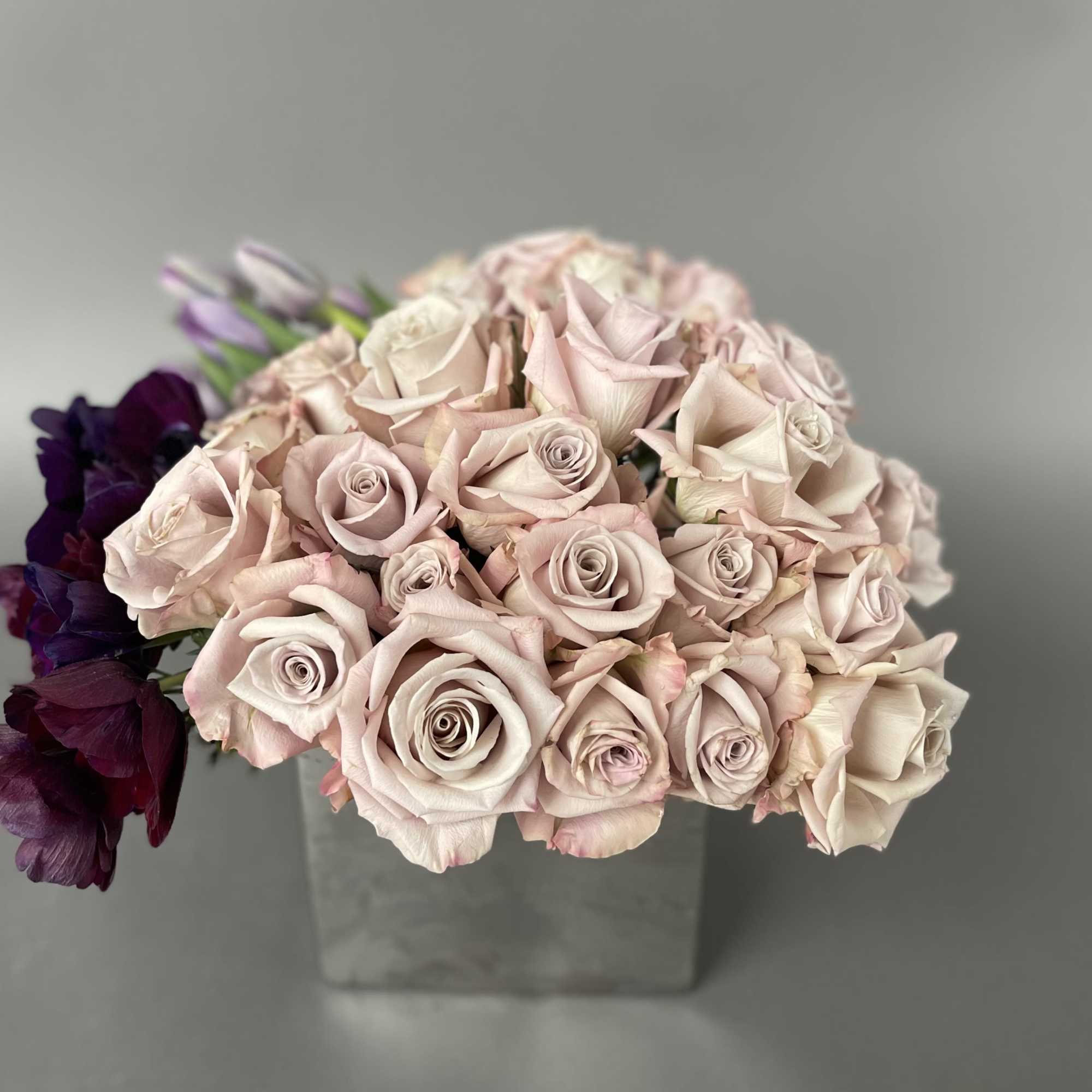 Bouquet of pale pink roses with dark purple flowers in a square vase