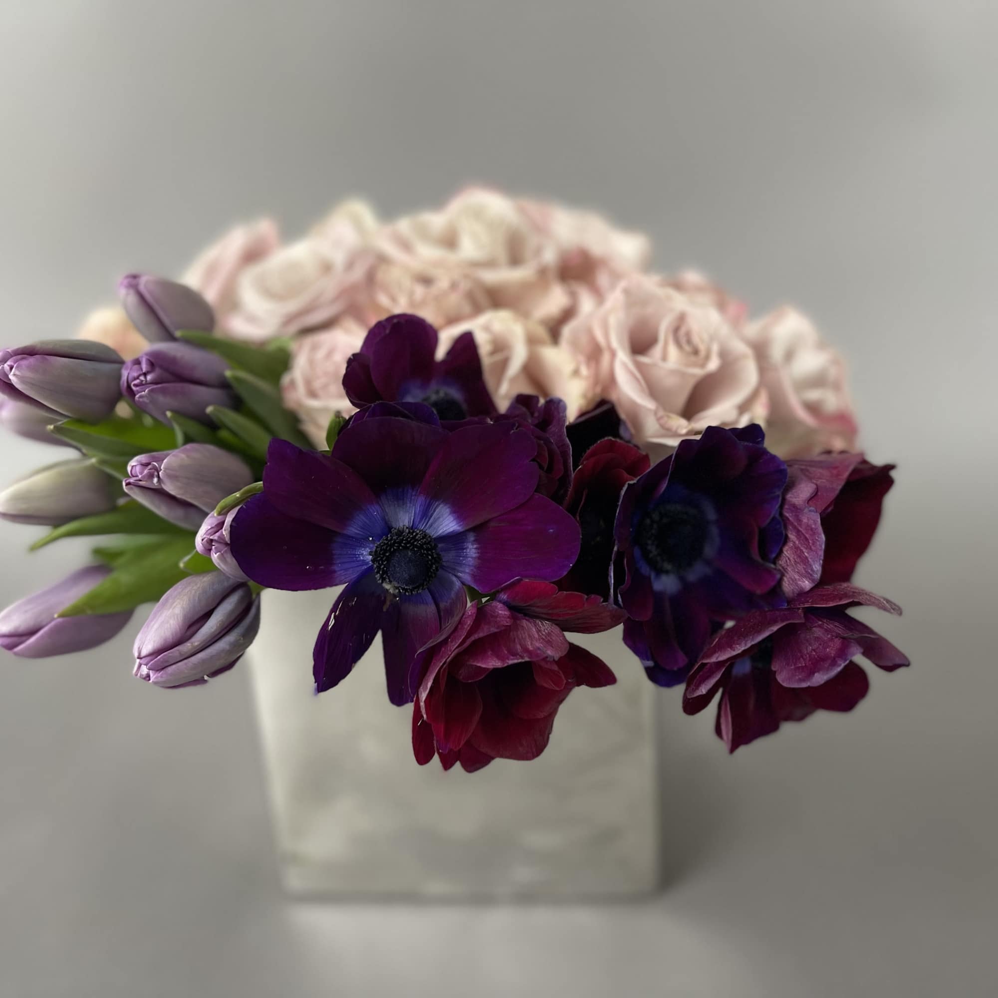 Purple anemones and lavender tulips in a white vase with pale pink roses