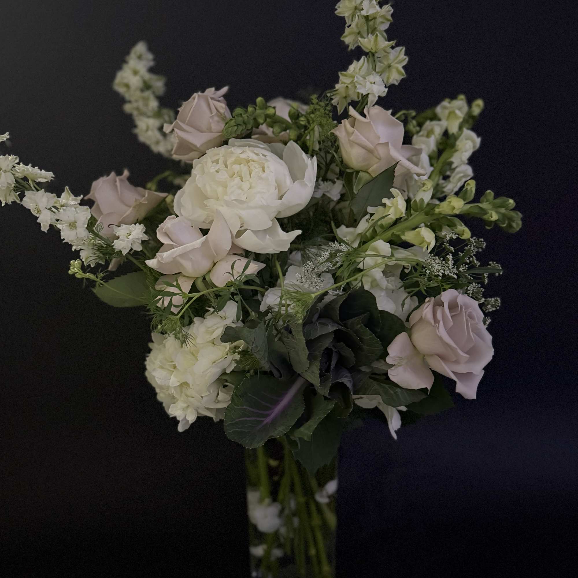 Tall vase arrangement of white peonies and hydrangeas with blush roses on a dark background