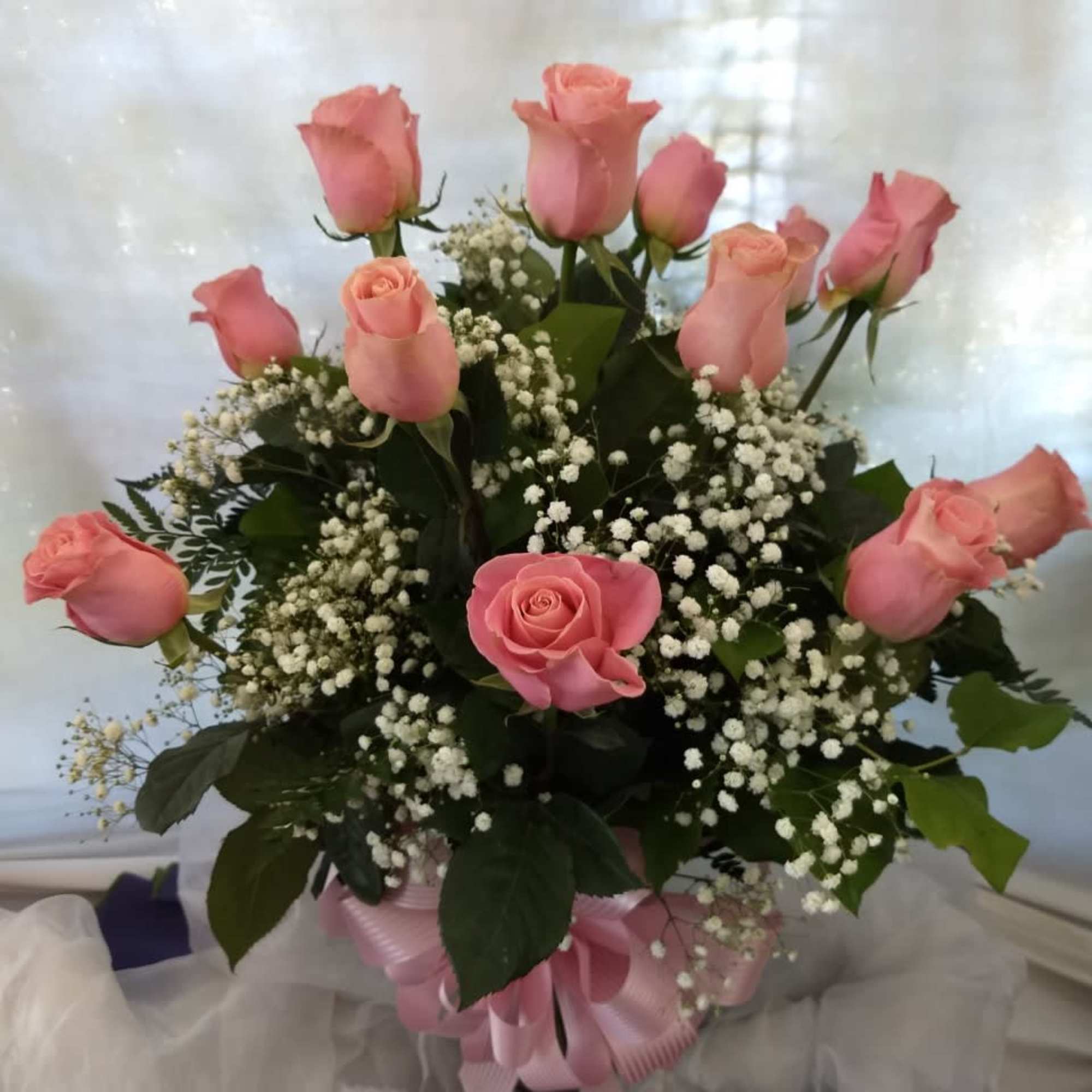 Pink roses arranged in a bouquet with baby's breath and a pink ribbon