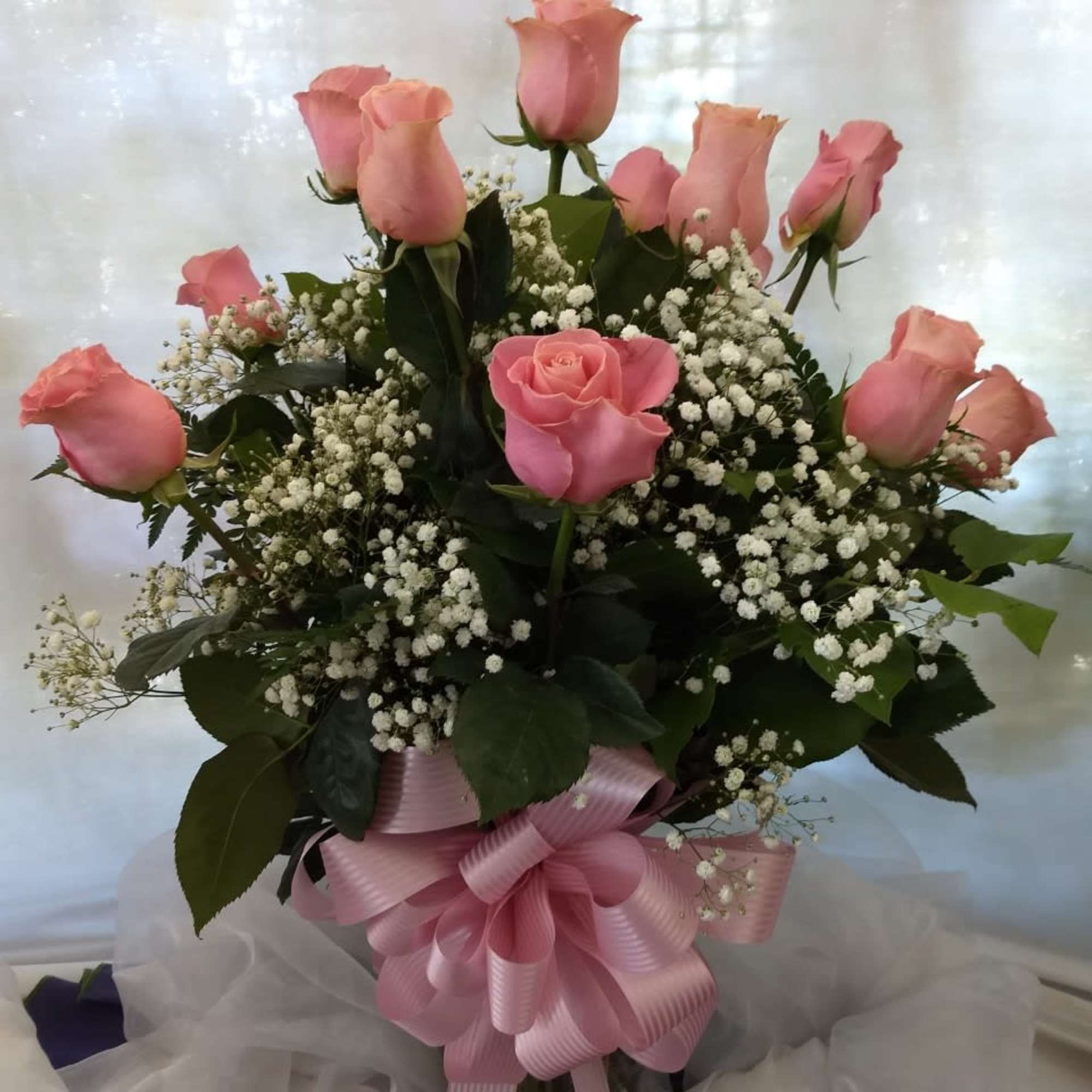 Pink roses arranged in a vase with baby's breath and a pink ribbon bow