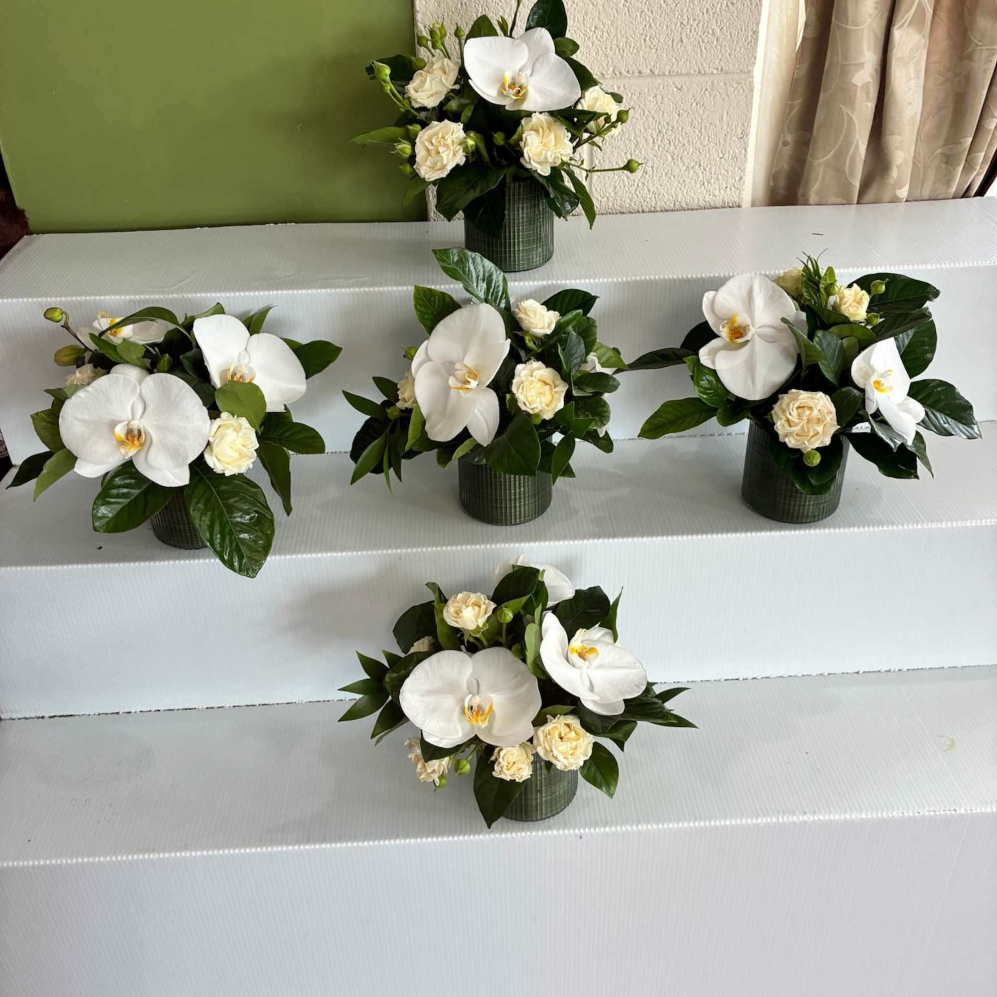 White orchid and cream rose arrangements in green containers