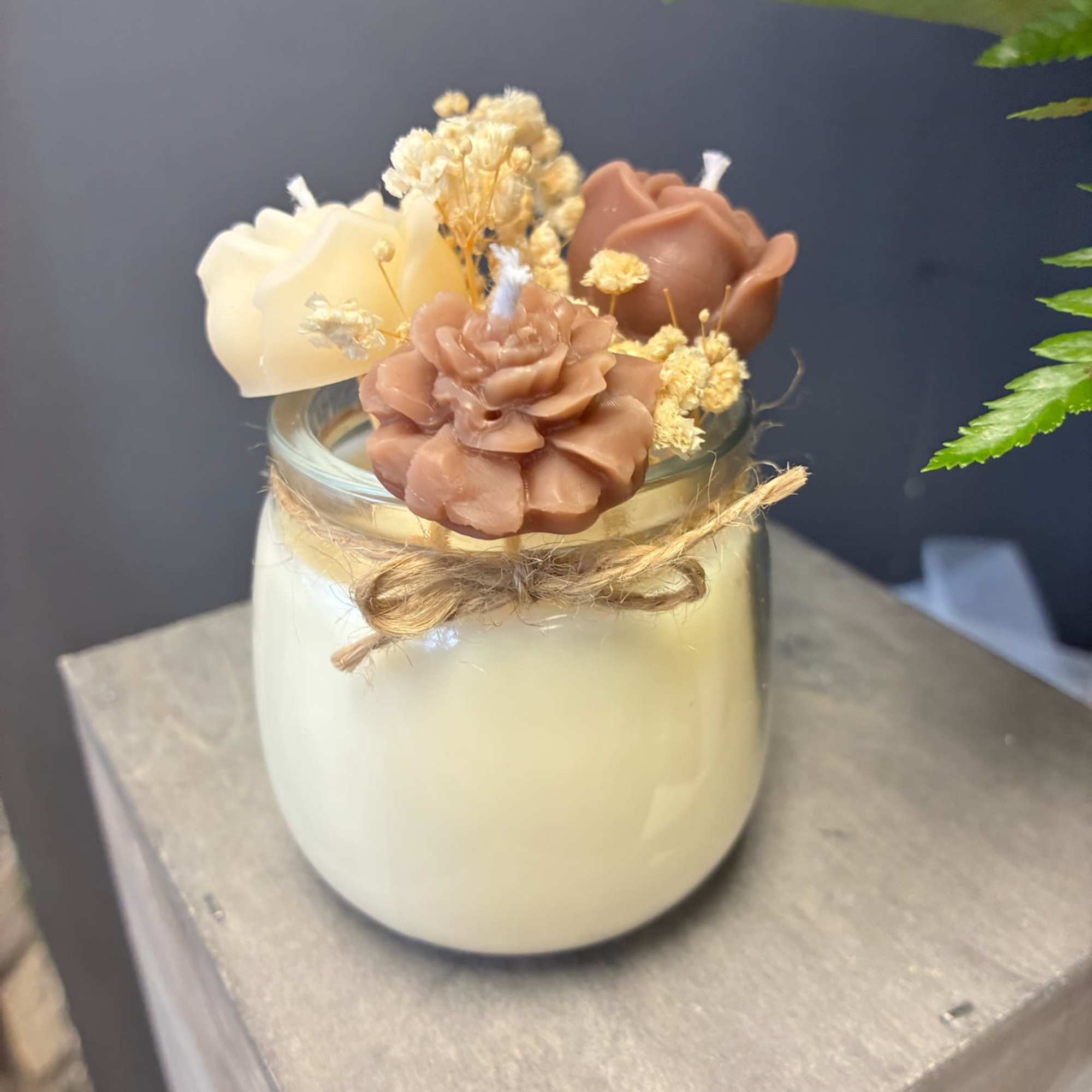 Small candle jar topped with decorative flowers and dried accents