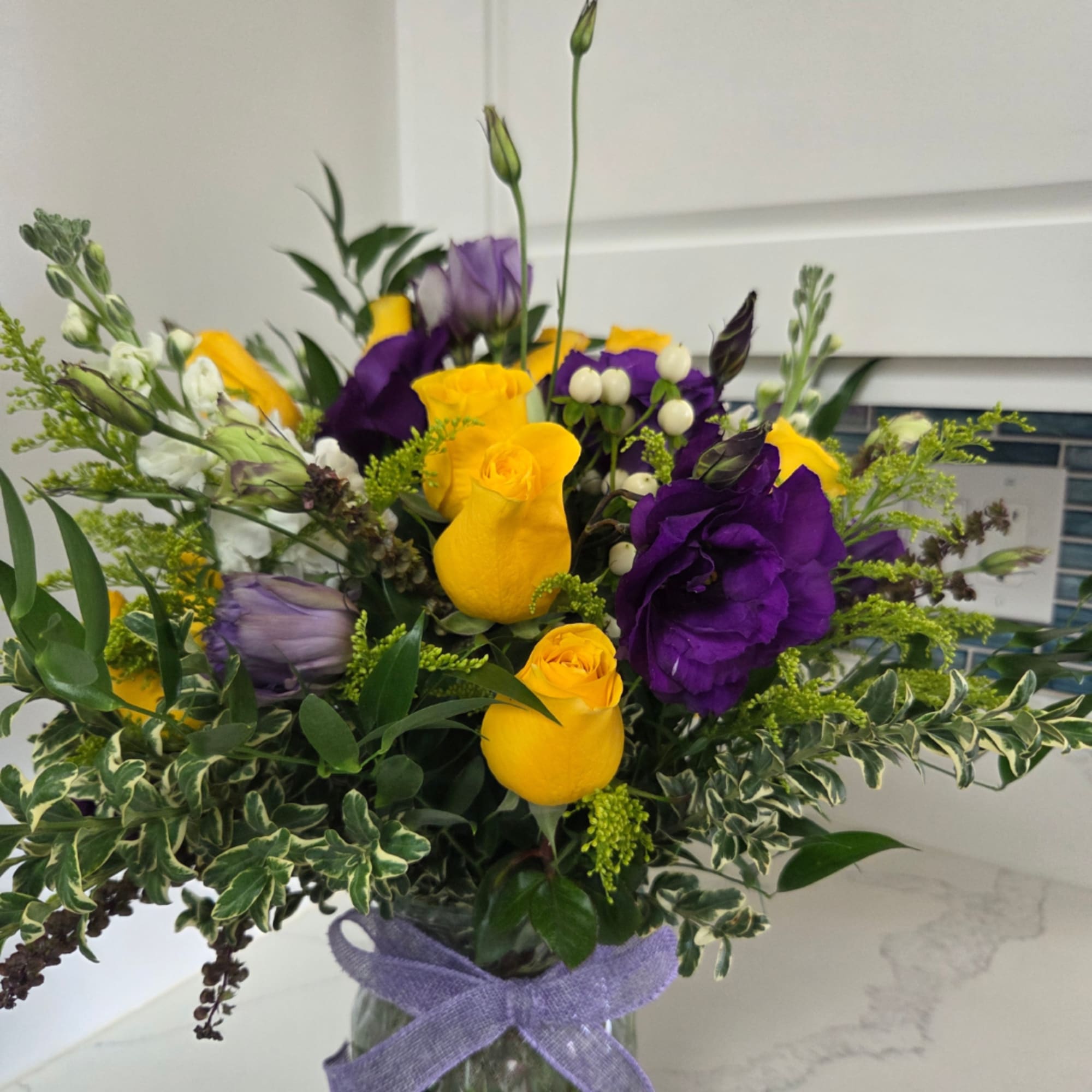 Bouquet of yellow and purple roses in a glass vase with a purple ribbon