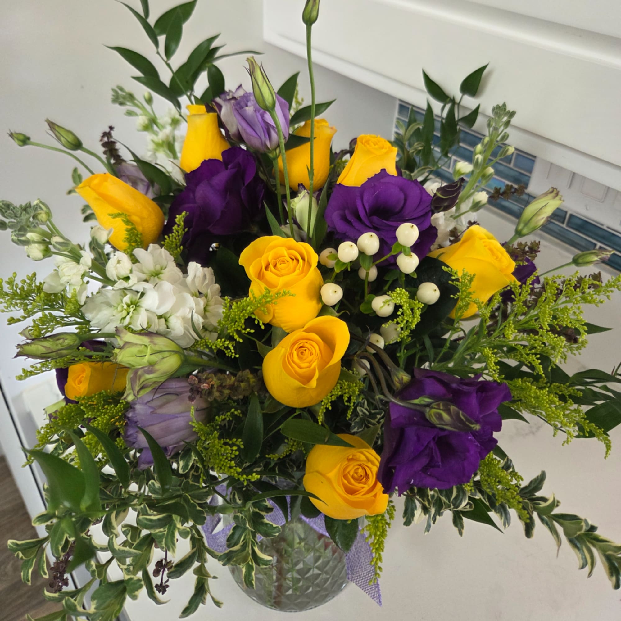 Yellow roses and purple lisianthus in a glass vase
