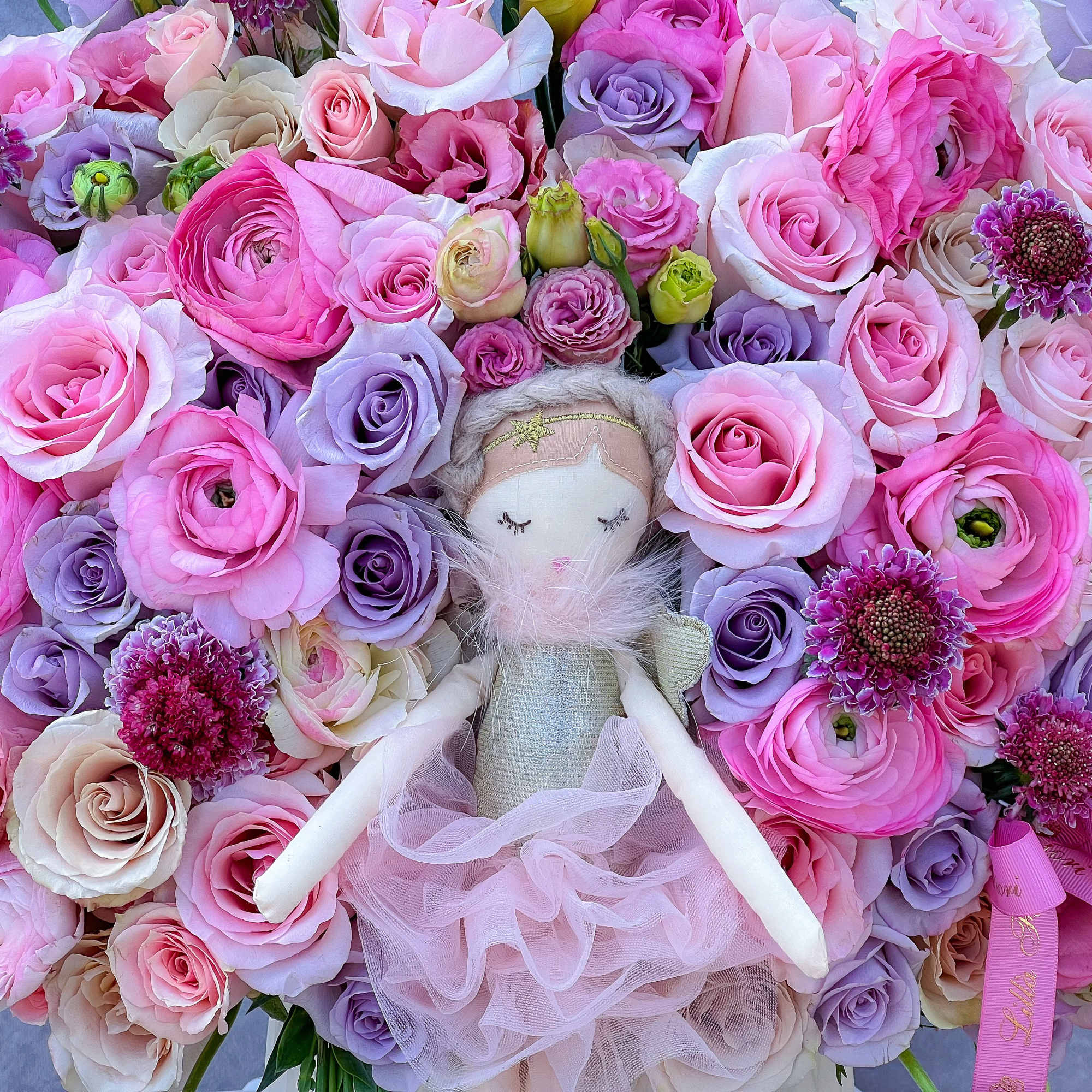 Pink and lavender rose bouquet with a small doll in the center