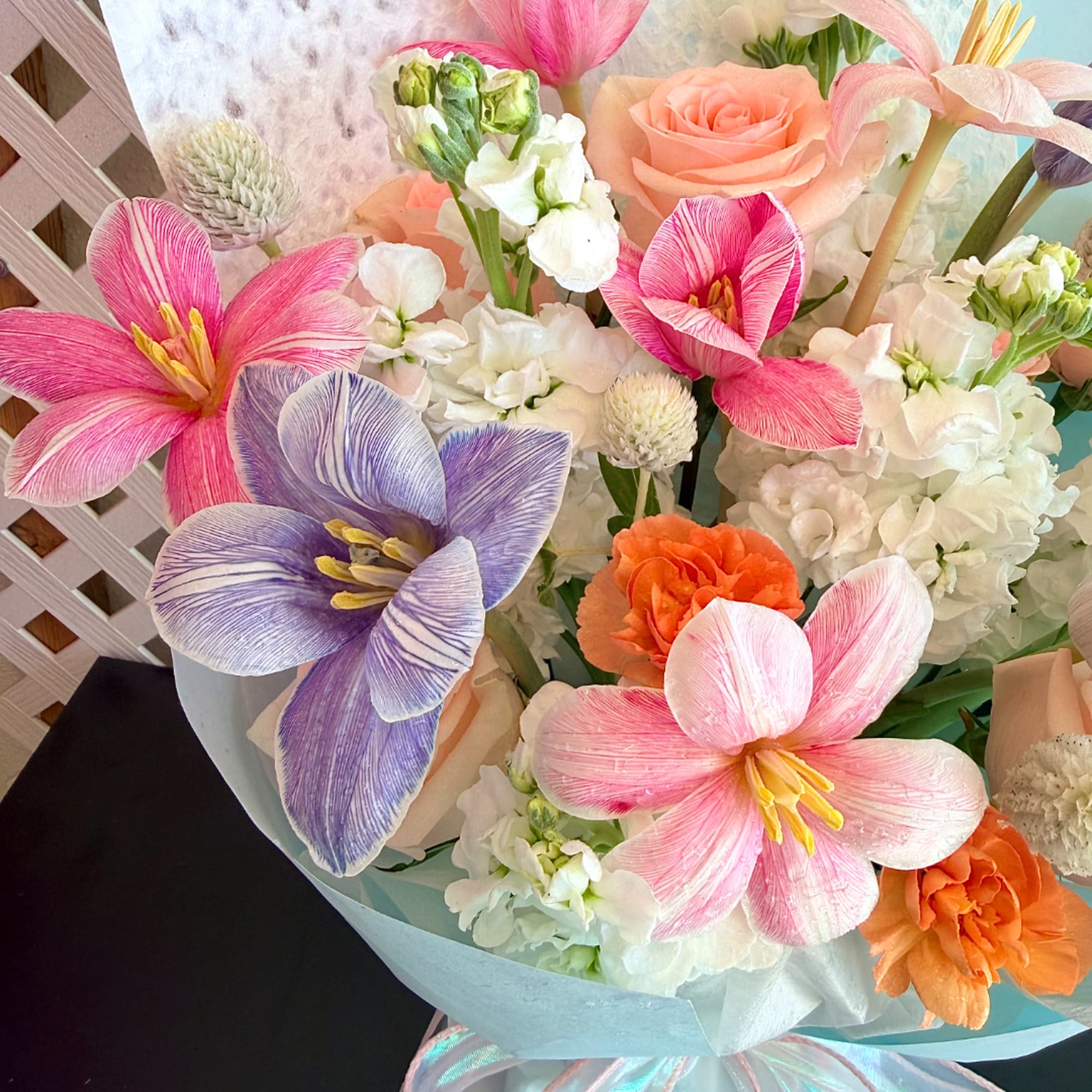 Bouquet of pink, purple, peach, and white flowers wrapped in pale blue paper