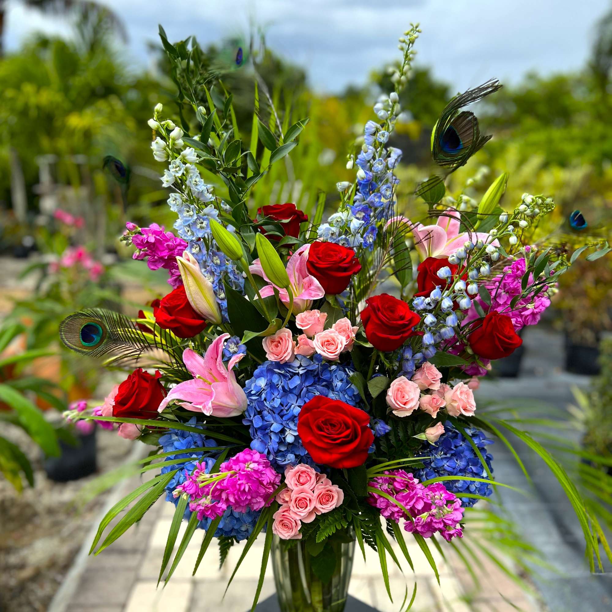 Tall bouquet of red roses, pink lilies, and blue flowers in a glass vase
