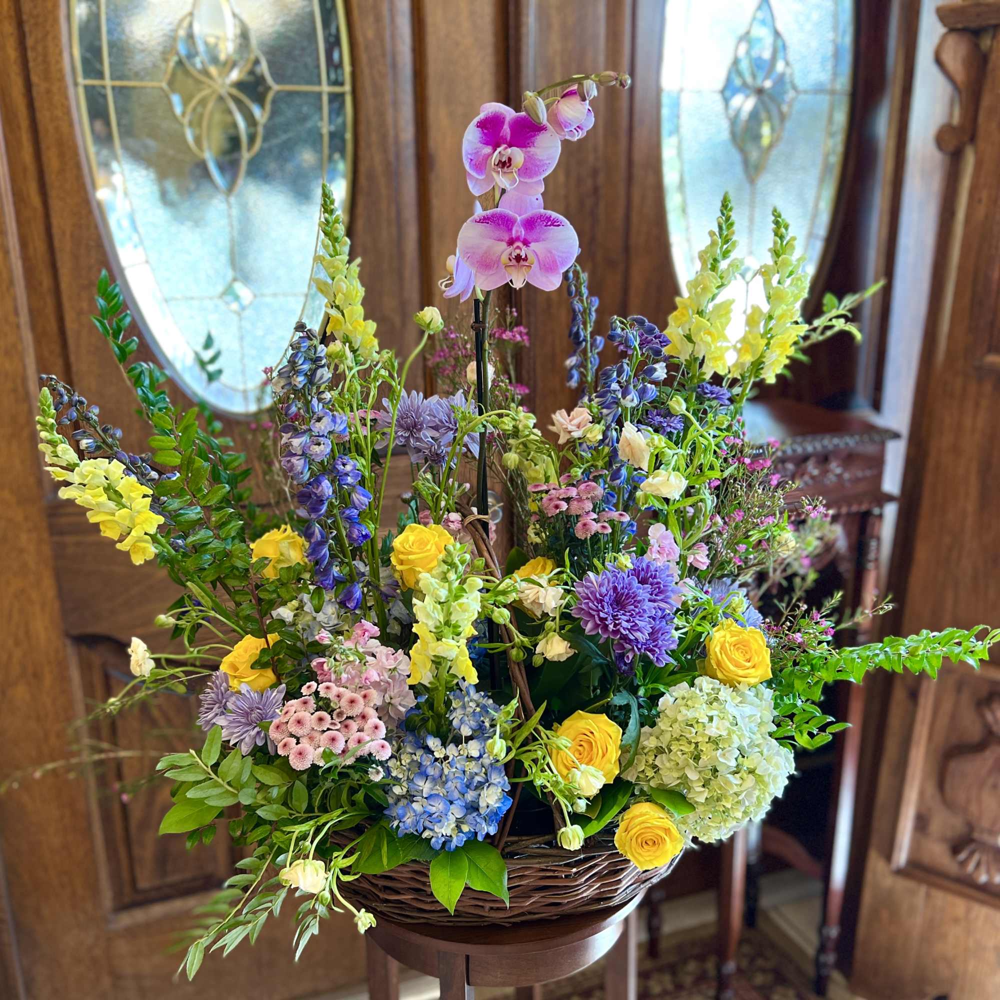 Large mixed flower arrangement with orchids, roses, and snapdragons in a wicker basket