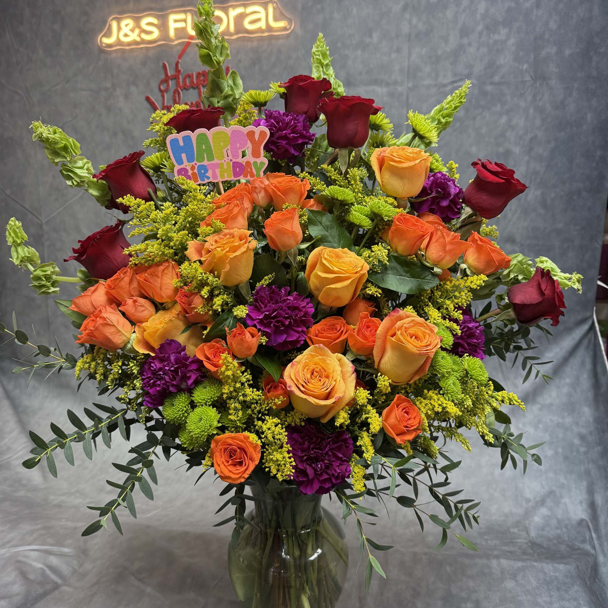 Large mixed bouquet of roses, carnations, and greenery in a glass vase