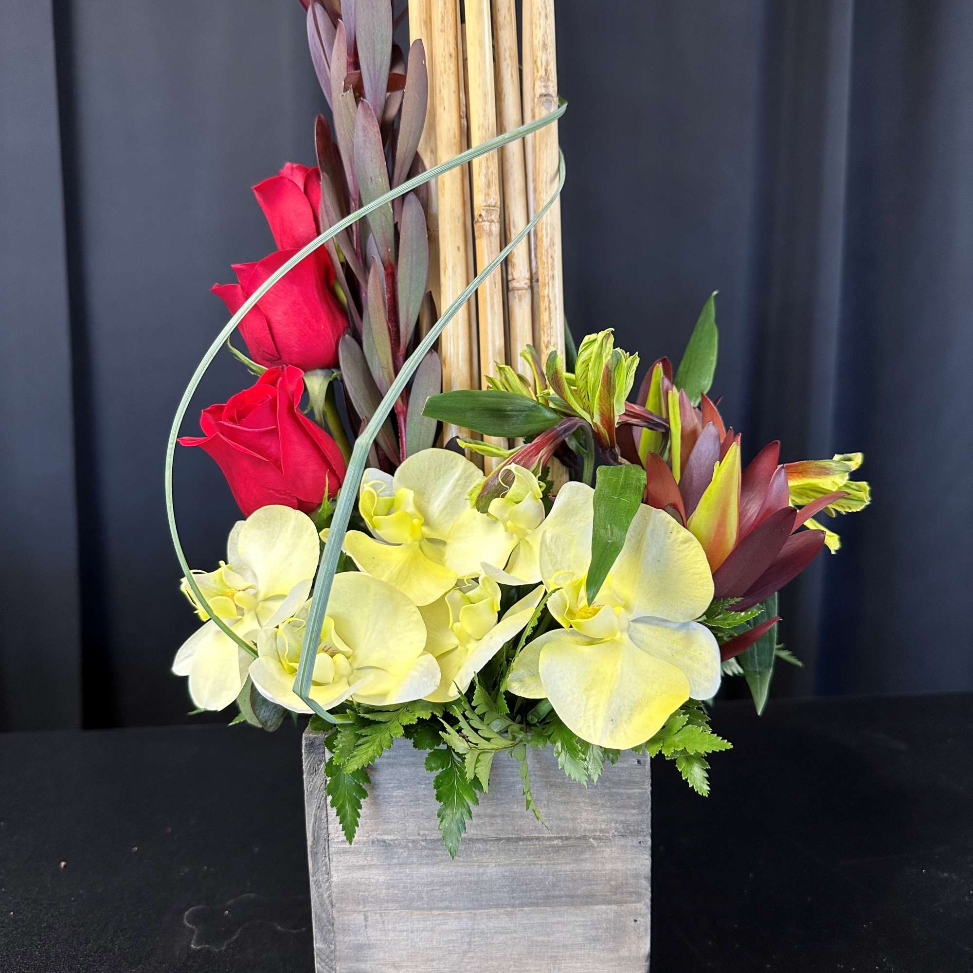 Red roses and pale yellow orchids in a square wooden container