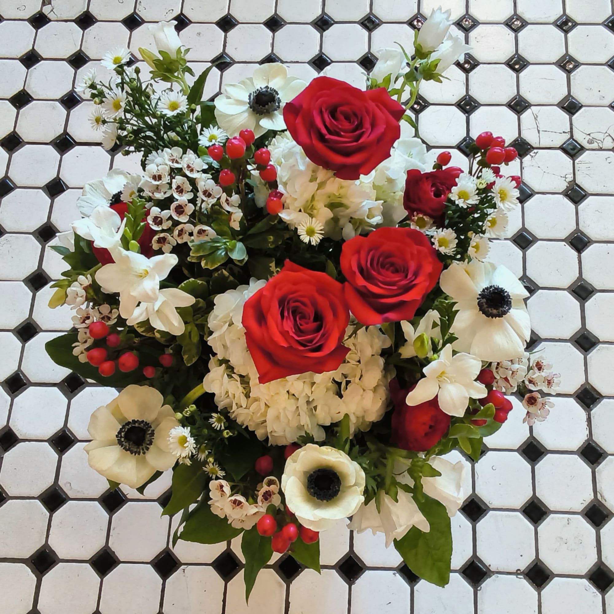 Round bouquet with red roses and white flowers on a tiled floor